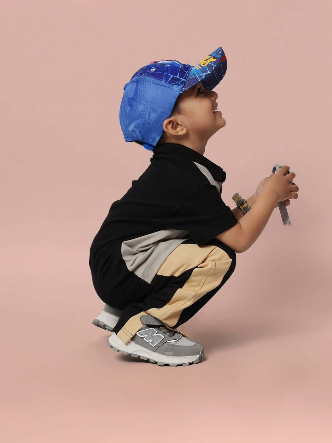 Young child wearing the TINGE SHIRT FOR BOYS & GIRLS GREY-BLACK, kneeling down, smiling, against a plain backdrop.