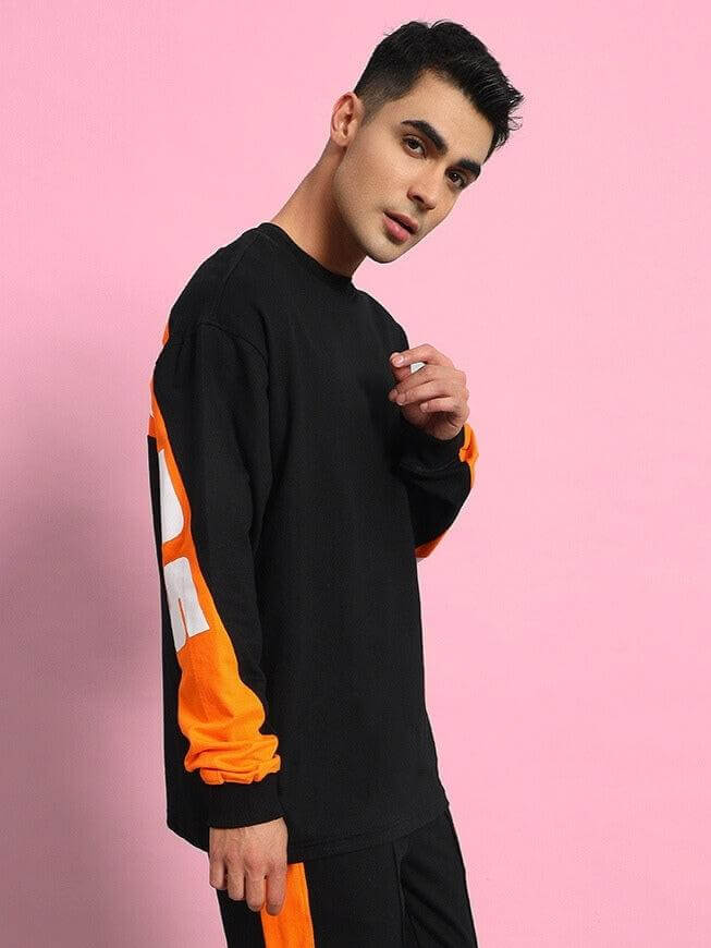 Model wearing TITAN oversized black sweatshirt with orange and white sleeve detail, made of premium cotton French terry lycra blend.