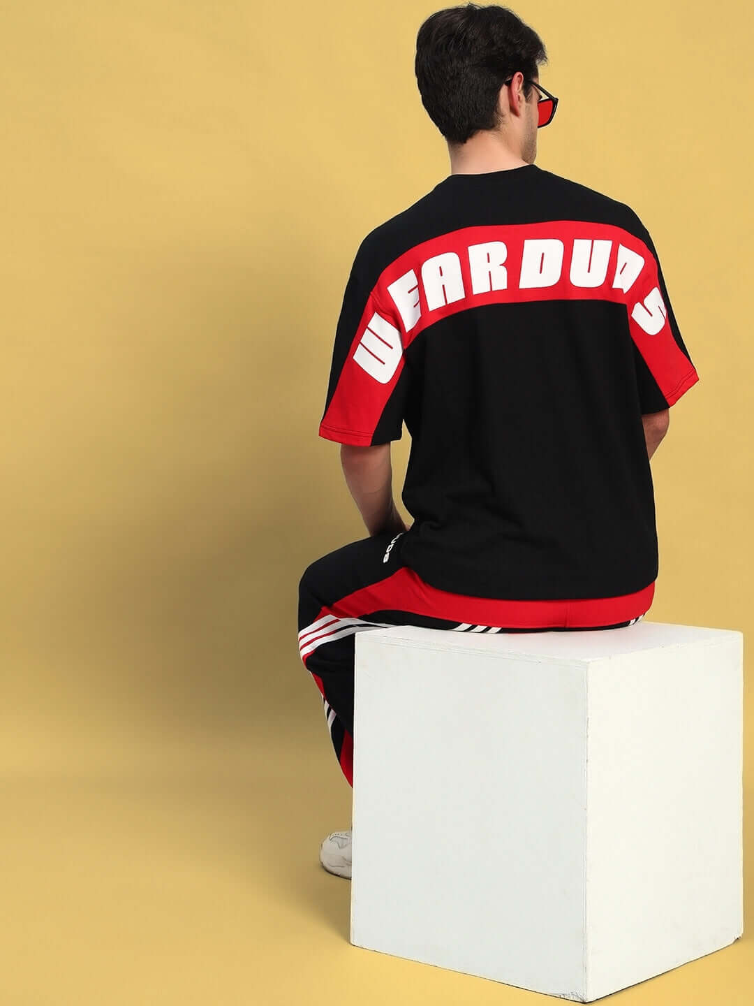 Model wearing TITAN oversized T-shirt in black and red, featuring premium cotton fabric, sitting against a yellow background.