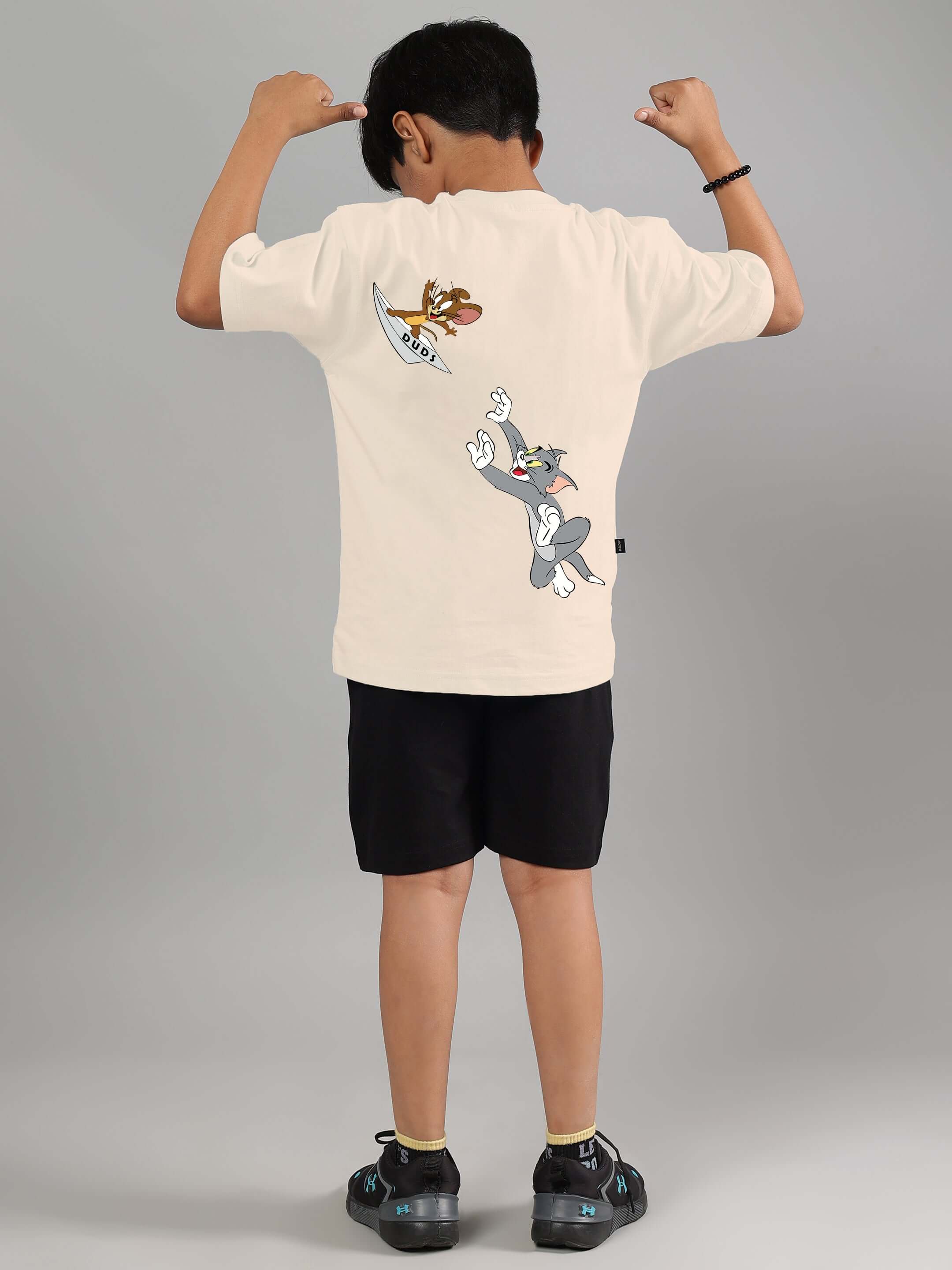 Boy wearing off-white Tom & Jerry co-ord with black shorts, featuring cartoon design on back, from DUDS.