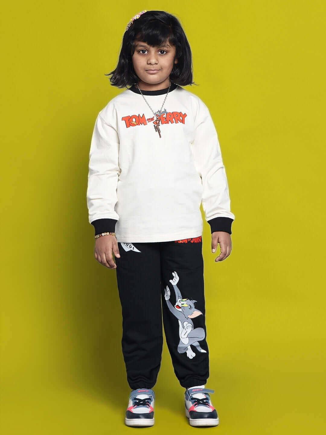 Child wearing Tom & Jerry oversized sweatshirt in off white and black with cartoon print, standing against a vibrant yellow background.