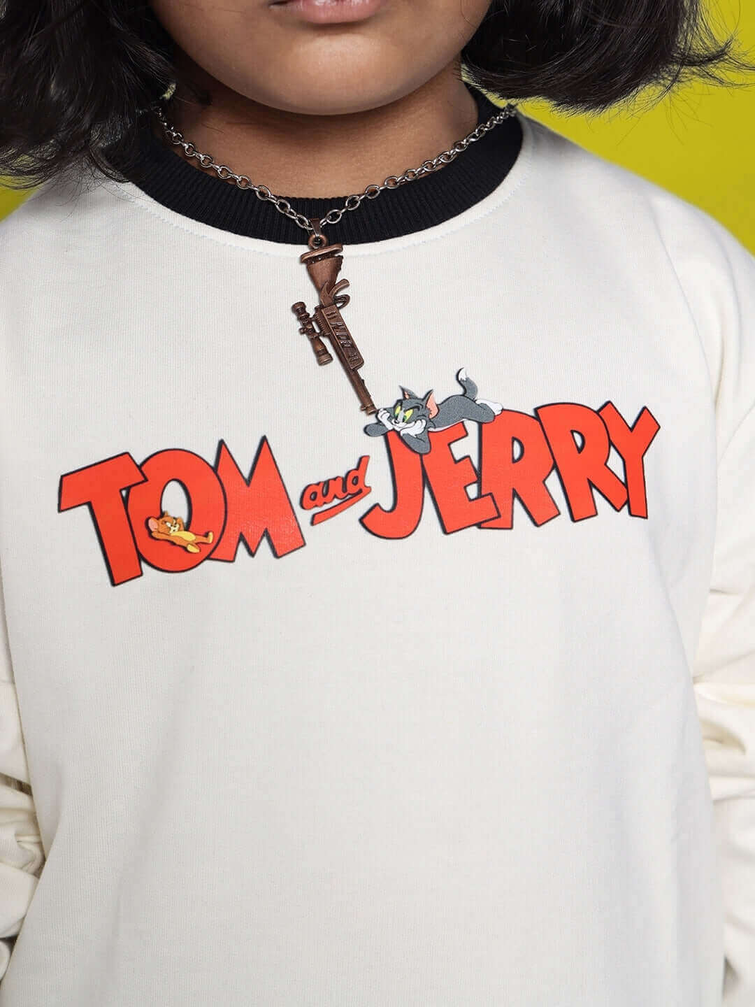 Close-up of off white-black Tom & Jerry oversized sweatshirt for kids, featuring bold red logo and cartoon characters.