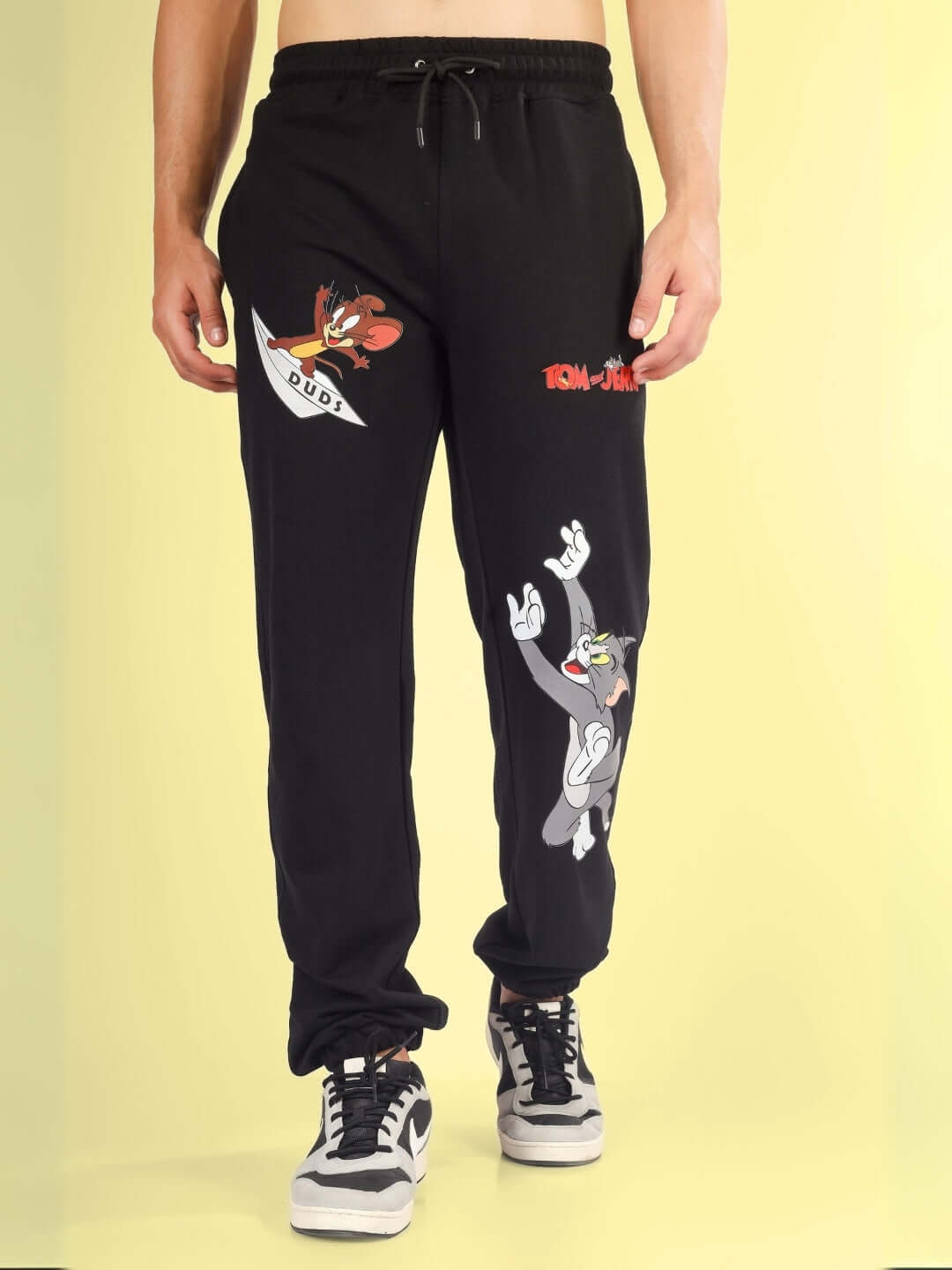 Person wearing black Tom & Jerry relaxed jogger pants with animated characters by DUDS.