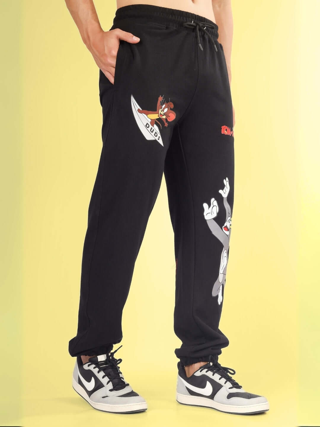 Person wearing TOM & JERRY Relaxed Jogger in black with custom fit and cartoon design by DUDS, offering 7-10 days dispatch shipping.