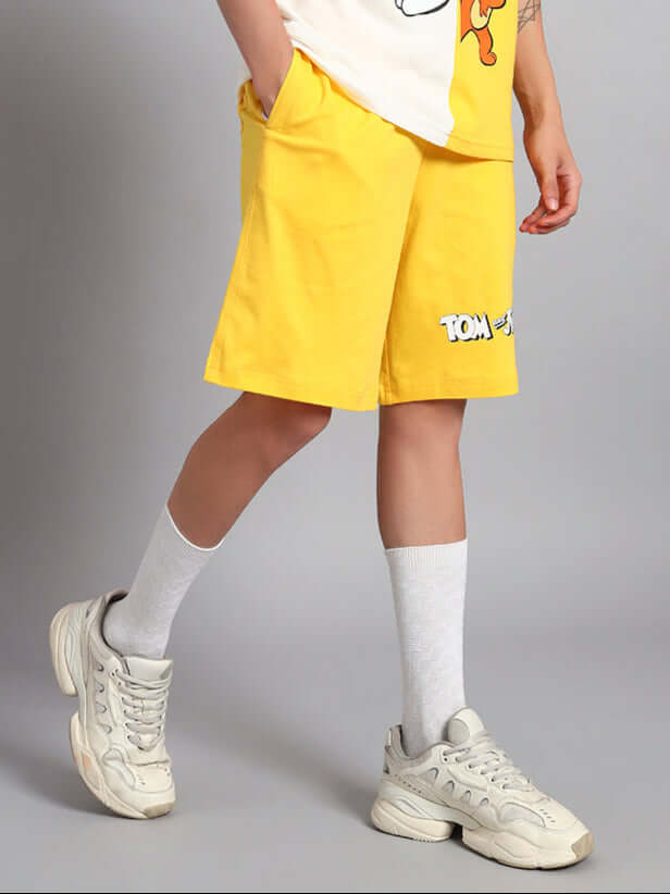 Person wearing Tom & Jerry yellow summer shorts with white sneakers.