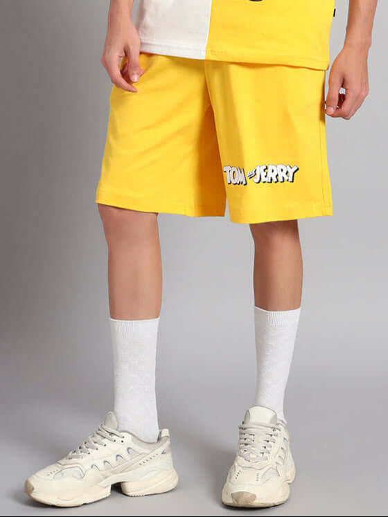 Person wearing TOM & JERRY yellow summer shorts, white socks, and sneakers, showcasing casual style.