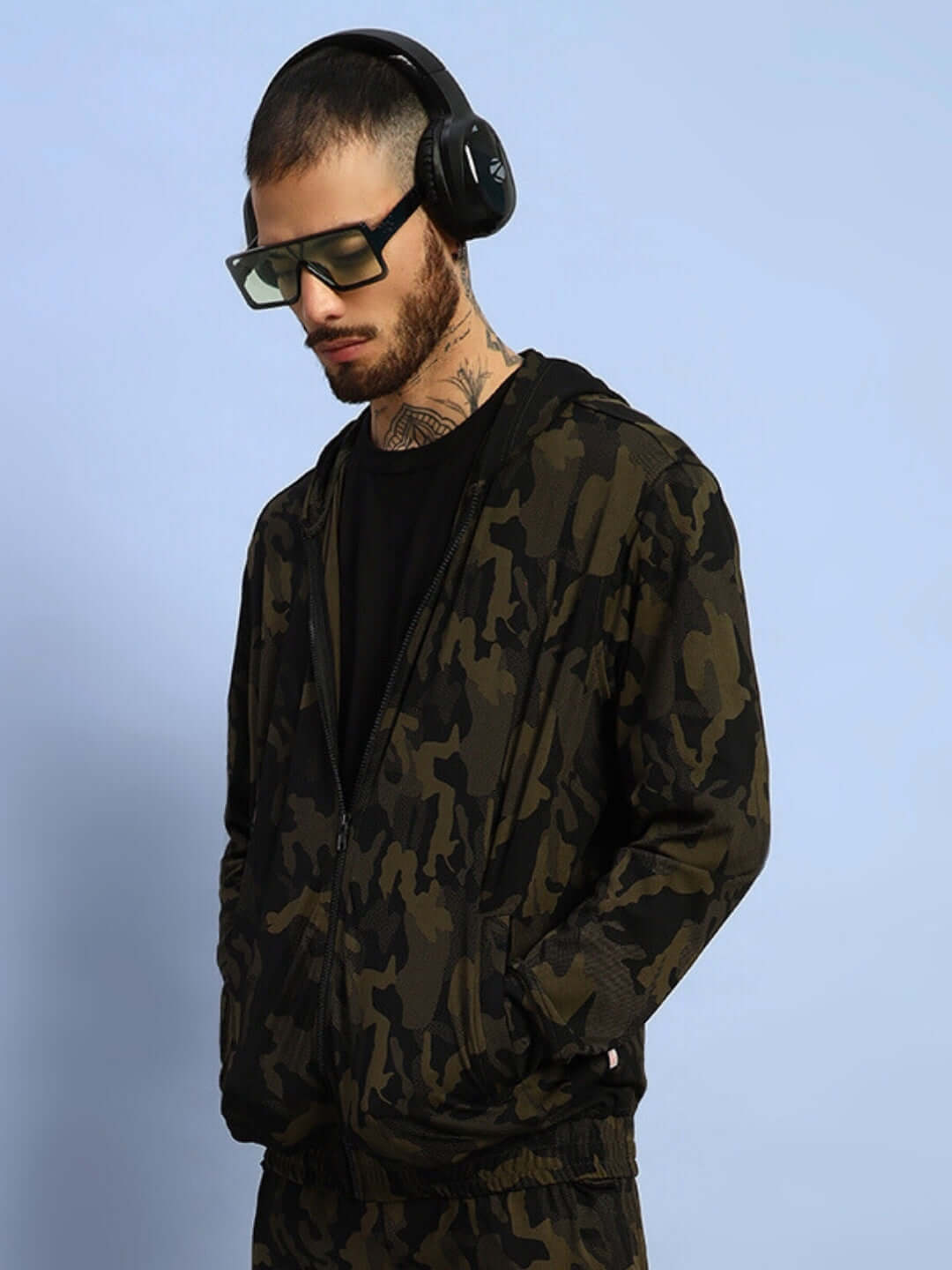 Man wearing trendy camo green jacket with headphones and sunglasses.