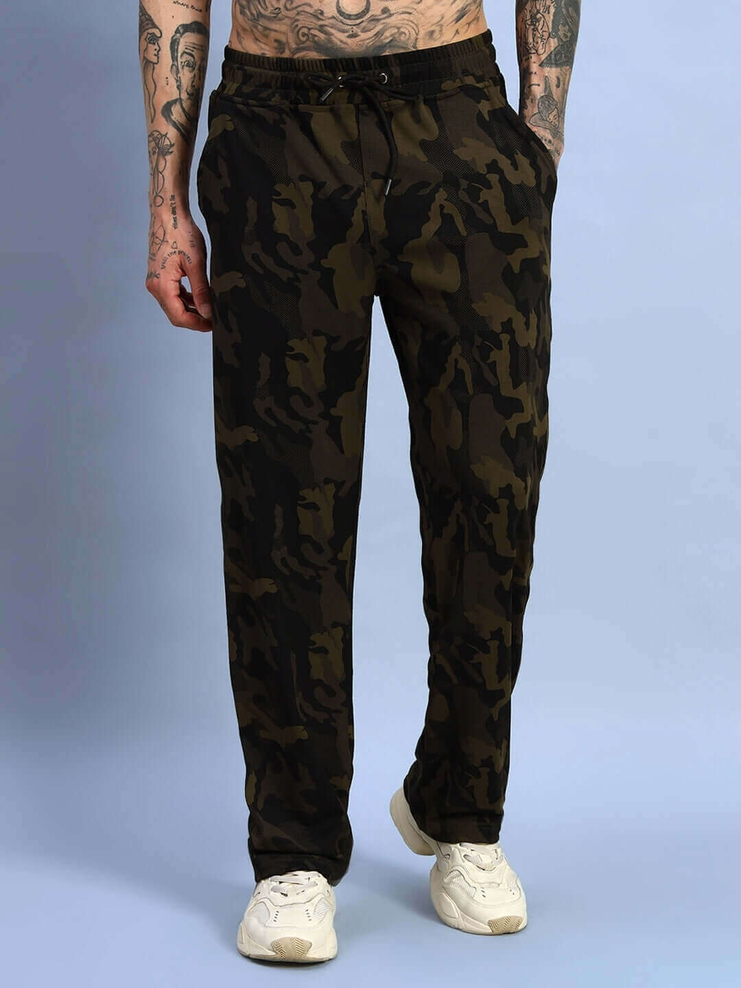 Model wearing Trench Relaxed Pant Jogger in Camo Green with white sneakers, featuring a stylish camo pattern on a blue backdrop.