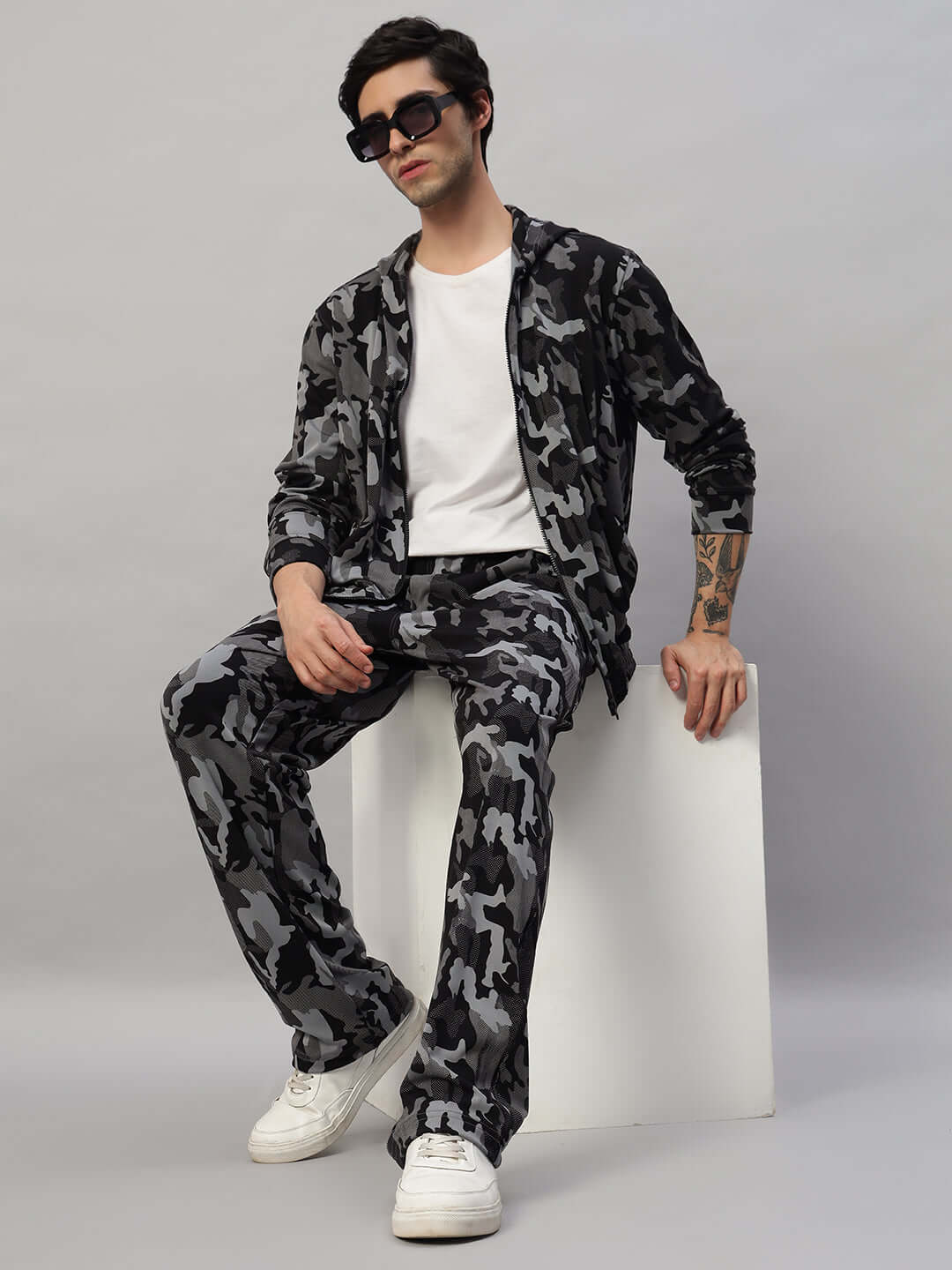 Model wearing a camo navy trench camouflage jacket by DUDS, made to order with custom fit option, sitting against a neutral backdrop.