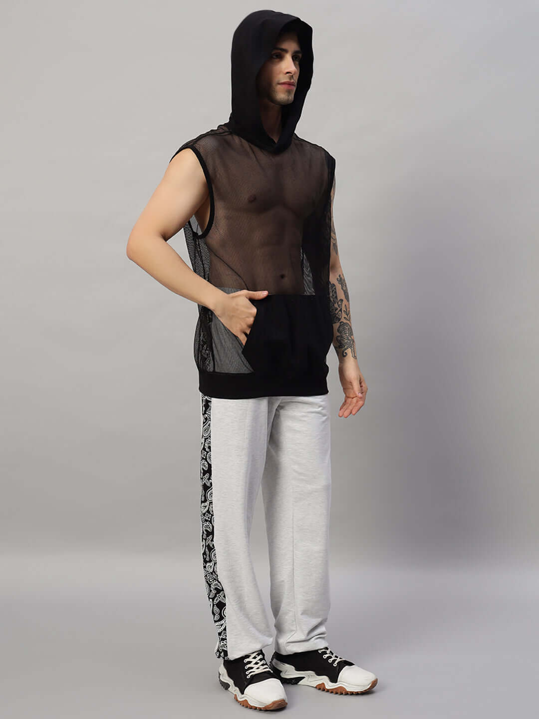 Man wearing mesh hoodie with printed side-stripe pants and sneakers, showcasing modern streetwear fashion.