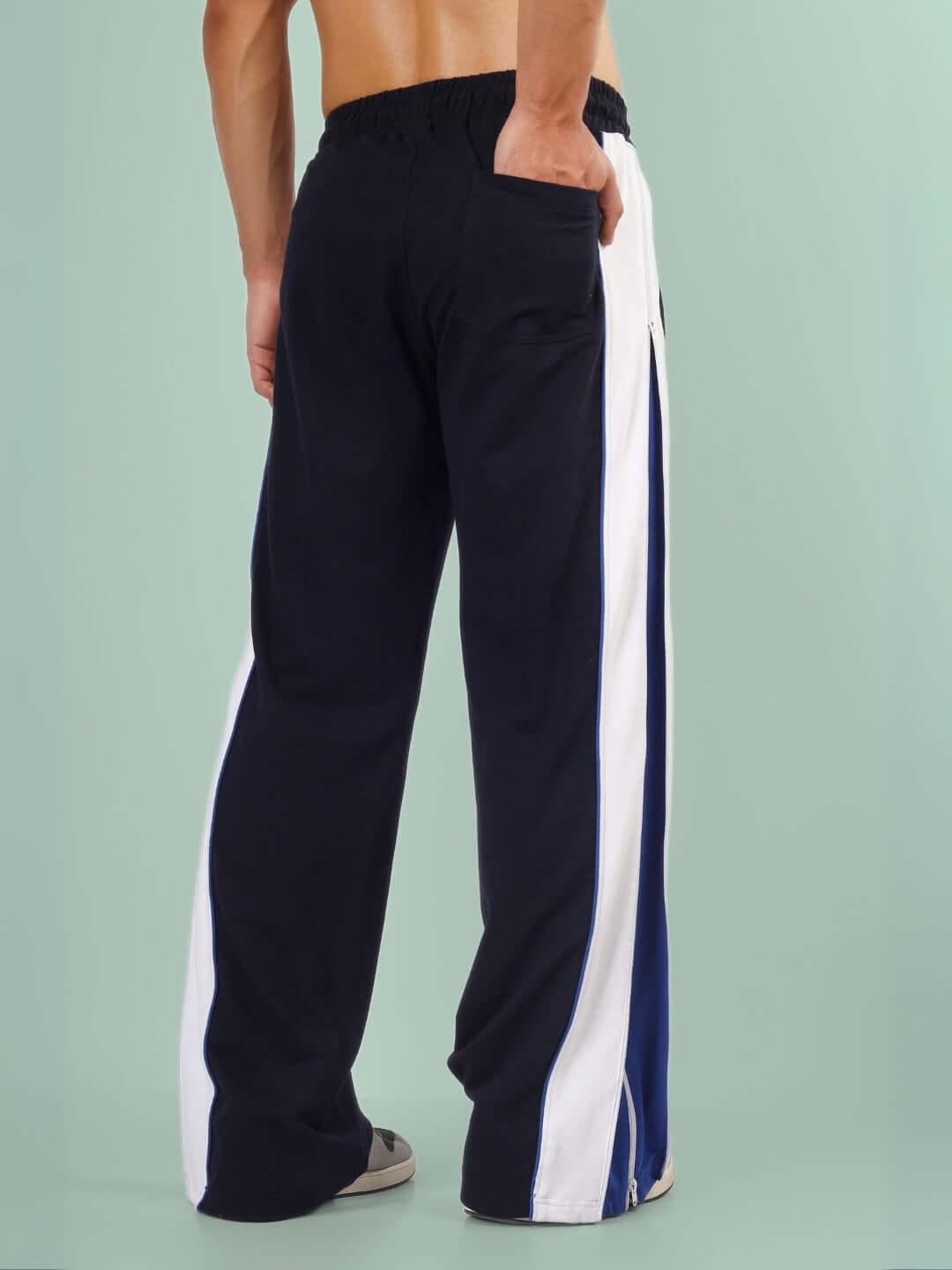 Back view of black joggers with blue and white side zippers, worn by a person, featuring a relaxed fit and elastic waistband.