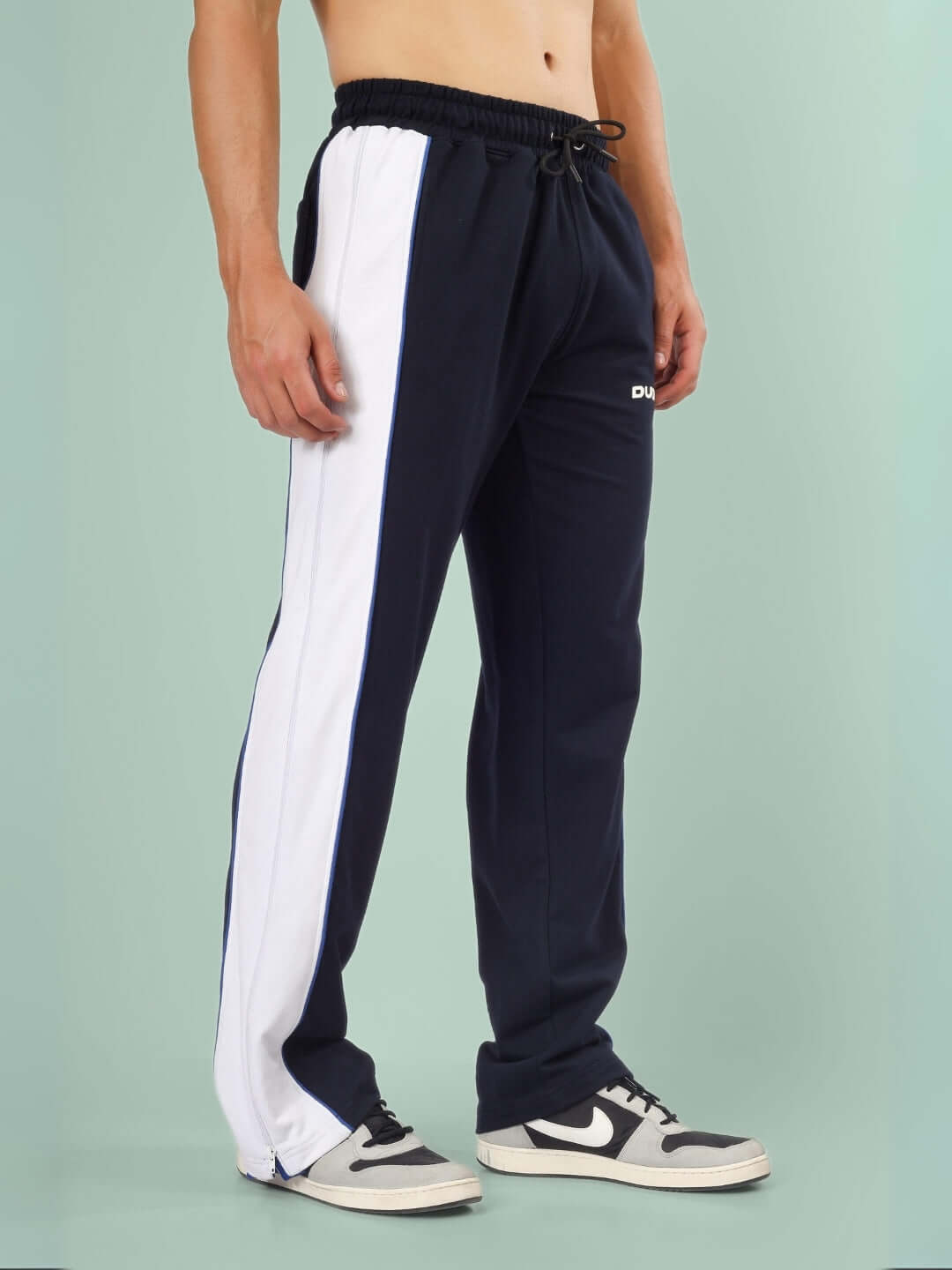 Model wearing TRIUMPH multi zipper joggers in black with blue and white side stripes, featuring custom fit option by DUDS.