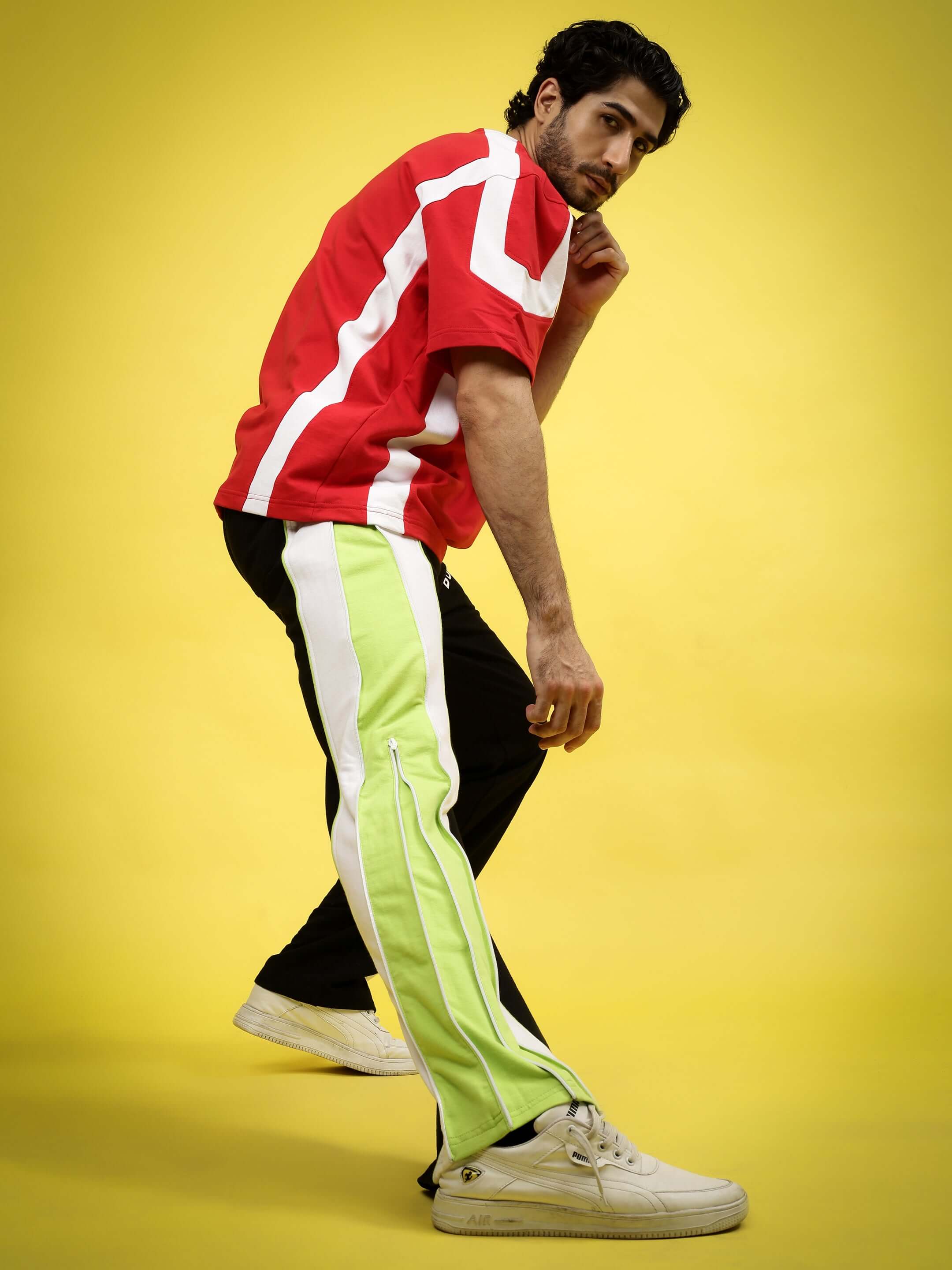 Model wearing TRIUMPH Multi Zipper Joggers in Black Neon with a red shirt against a yellow background.