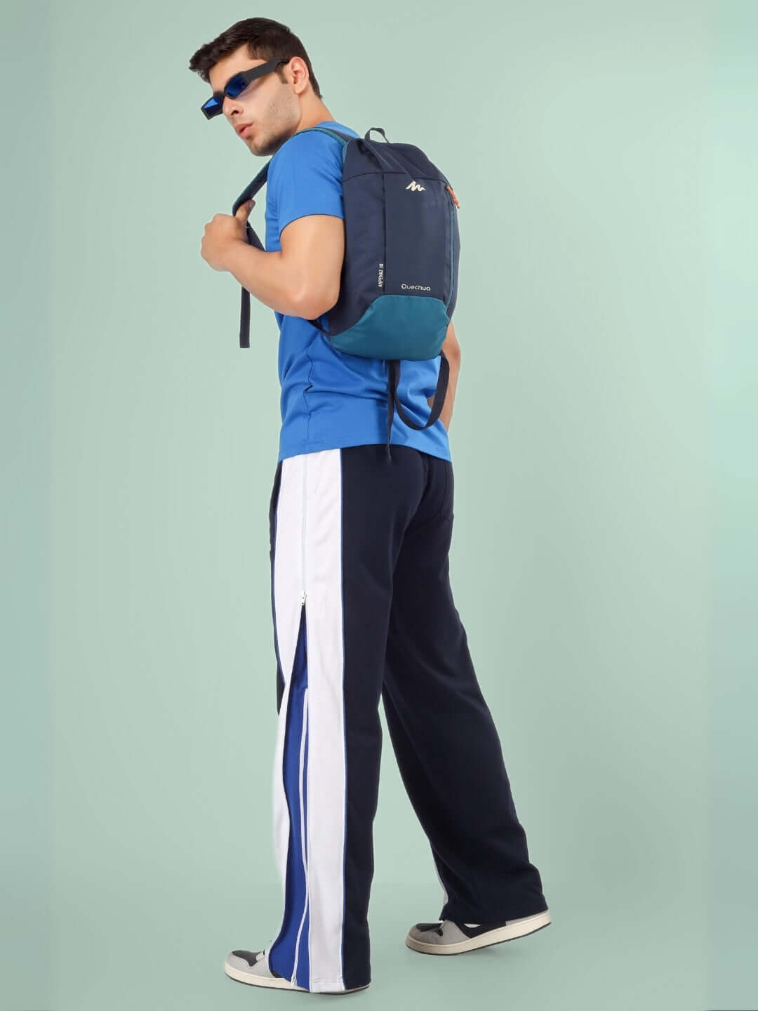 Man wearing black joggers with blue and white stripes, carrying a navy backpack and wearing sunglasses.
