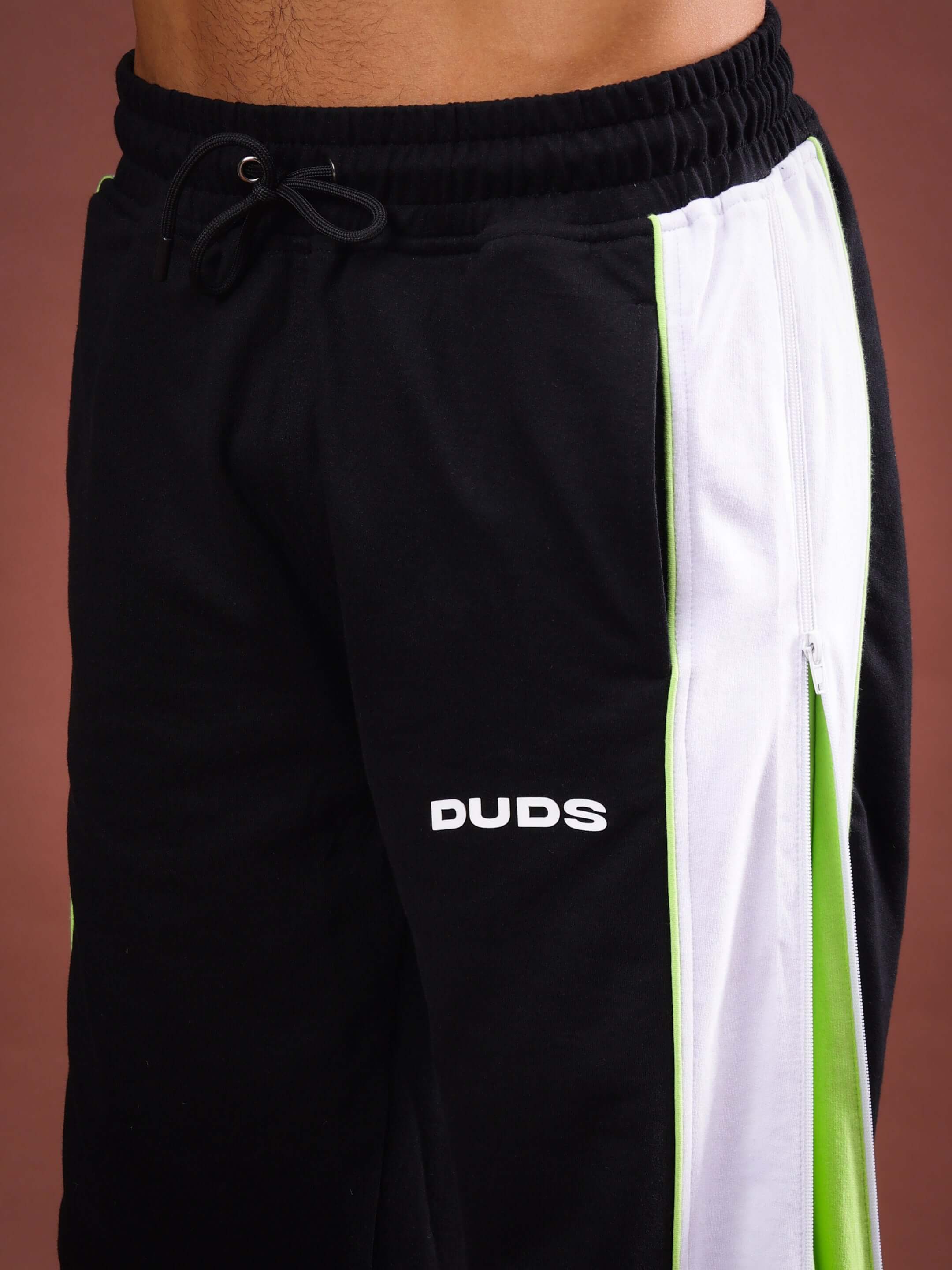 Close-up of black neon TRIUMPH joggers with multi zippers and DUDS logo, showcasing sleek design and vibrant accents.