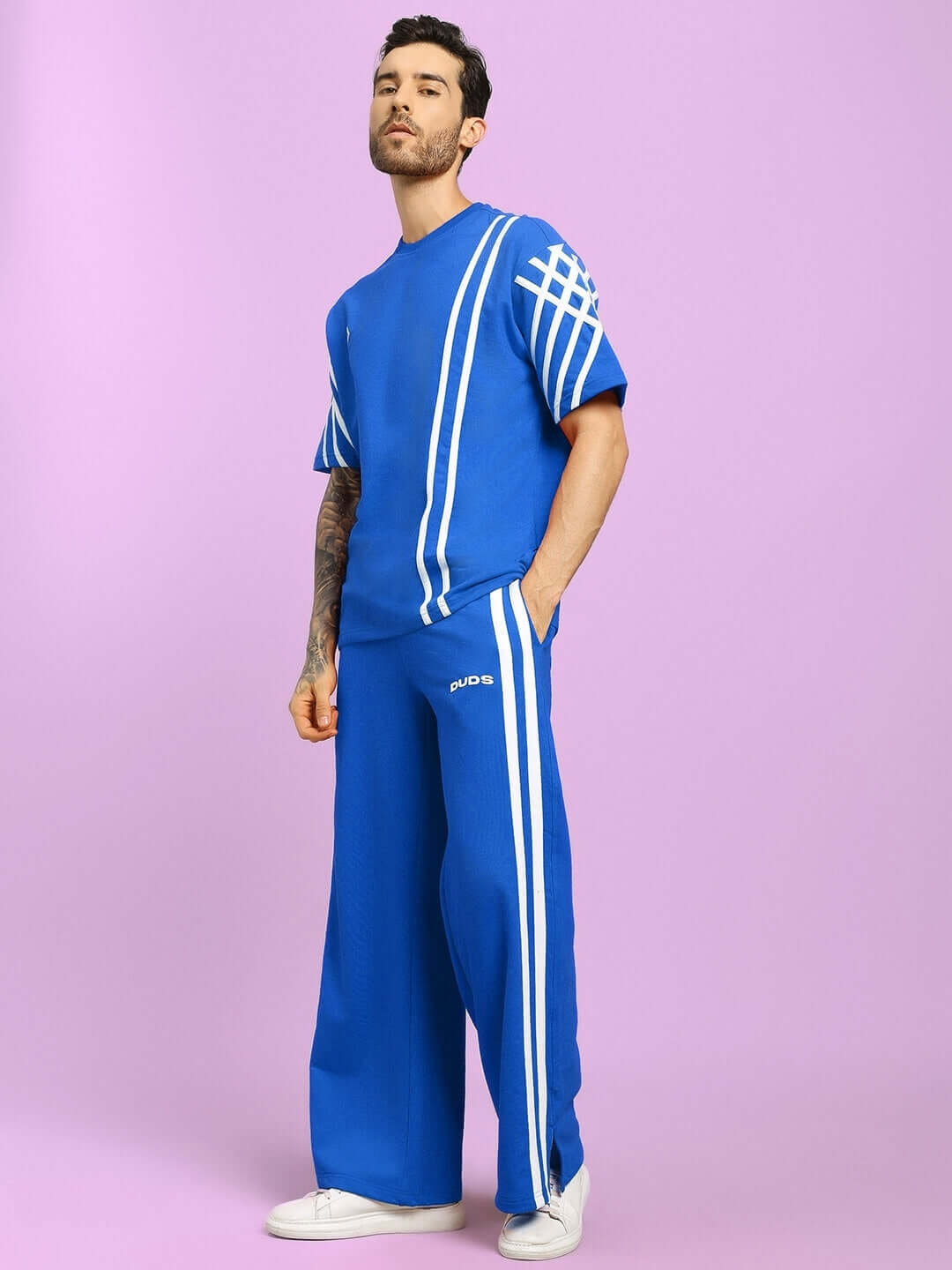 Man wearing a United Stripe Co-ord Set in blue, featuring premium heavy gauge fabric with white stripes, posing against a pink background.