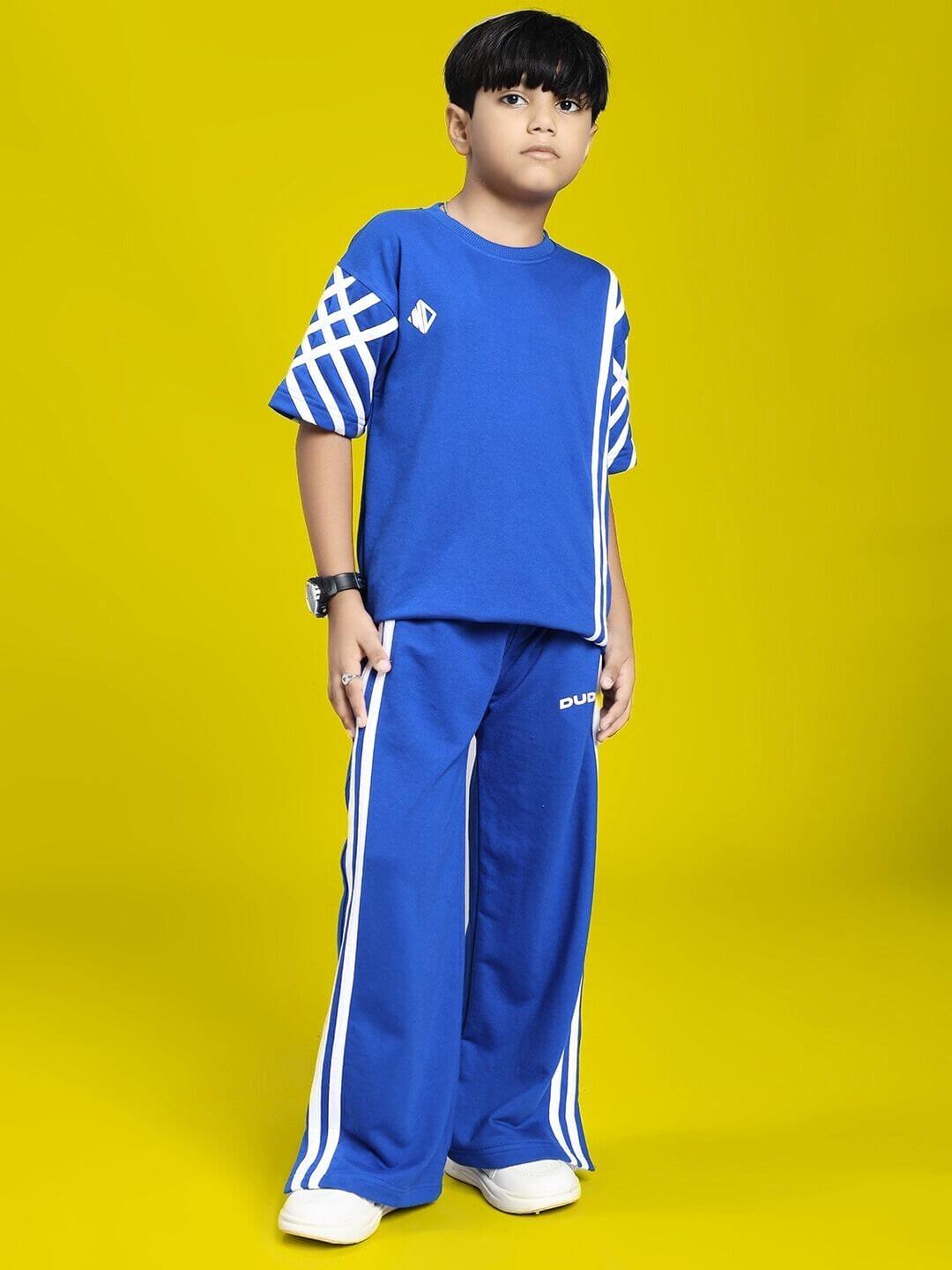 Boy wearing UNITED STRIPE CO-ORD SET FOR BOYS GIRLS BLUE with white sneakers against a yellow background.