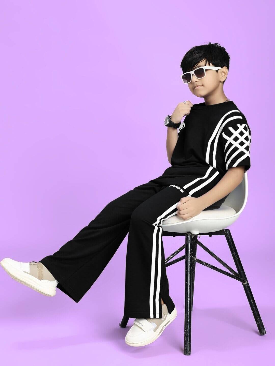 Child wearing UNITED STRIPE CO-ORD SET FOR BOYS GIRLS BLACK with sporty stripe details on a purple background, sitting on a chair.