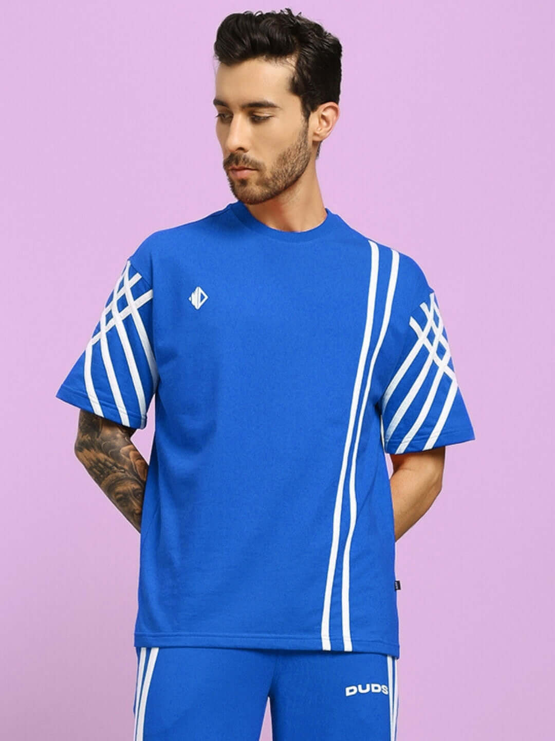 Model wearing blue UNITED STRIPE oversized t-shirt made from premium cotton blend, featuring white stripes, against a purple background.