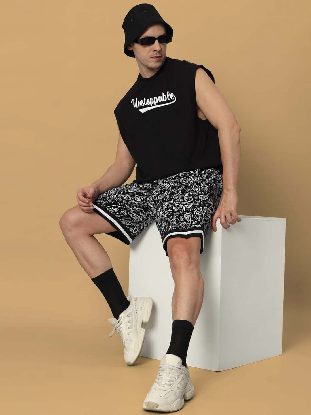 Man wearing Unstoppable Gym T-shirt in black with custom fit option, paired with patterned shorts, sitting in a casual pose.