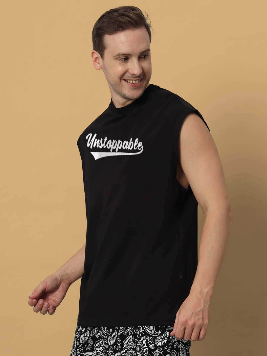 Man wearing an Unstoppable black gym T-shirt, smiles while posing against a beige background.
