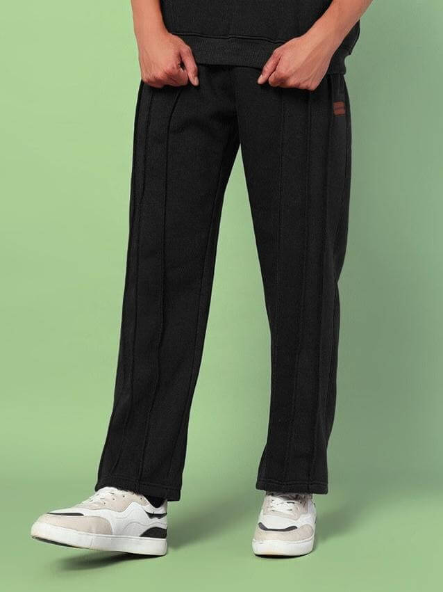 Model wearing URBAN FLEECE CARGO PANTS BLACK against green background, highlighting sleek black tone and relaxed silhouette.