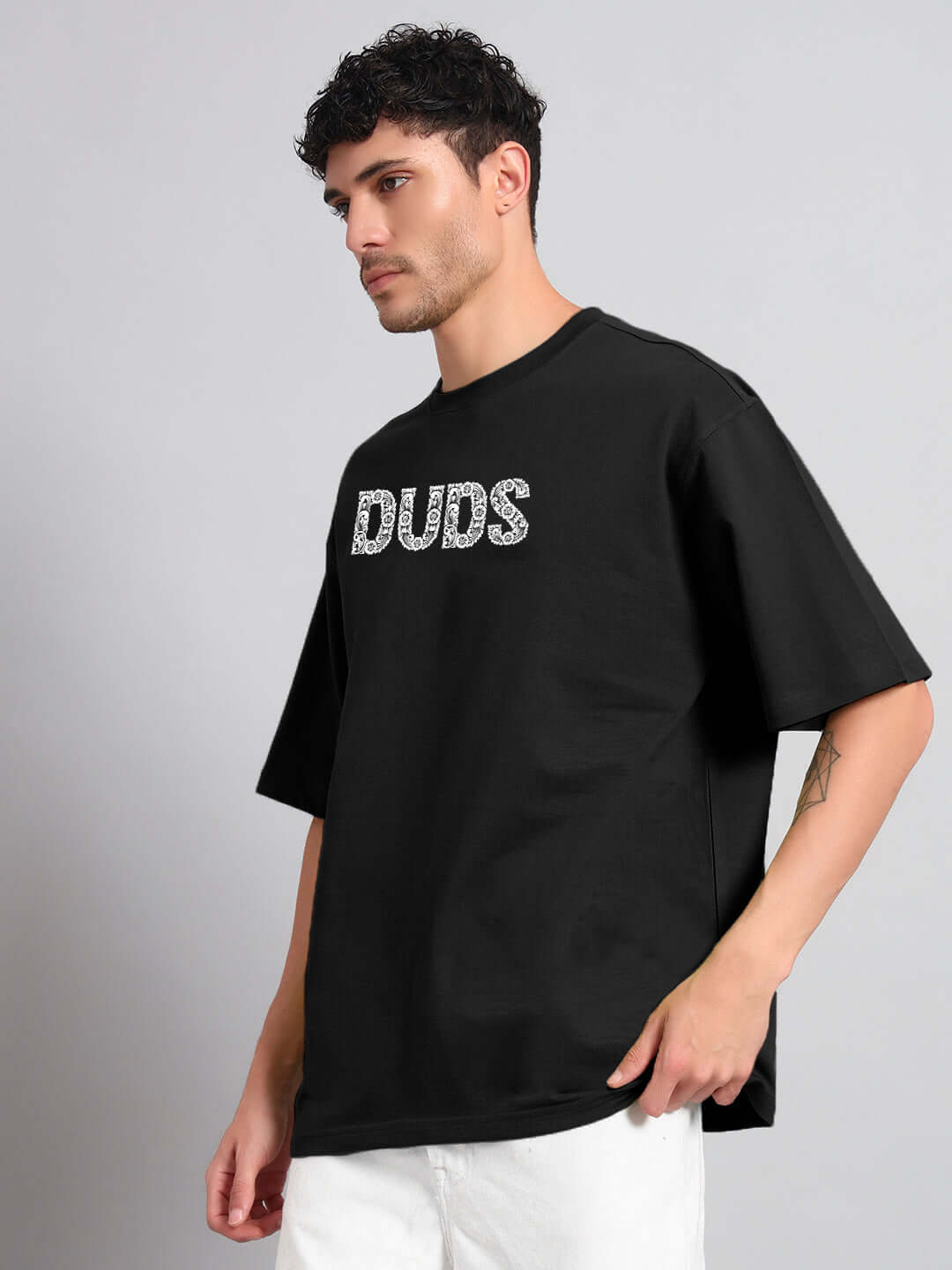 Man wearing URBAN PETAL OVERSIZED T-SHIRT BLACK, featuring relaxed fit and petal graphic, against a gray background.