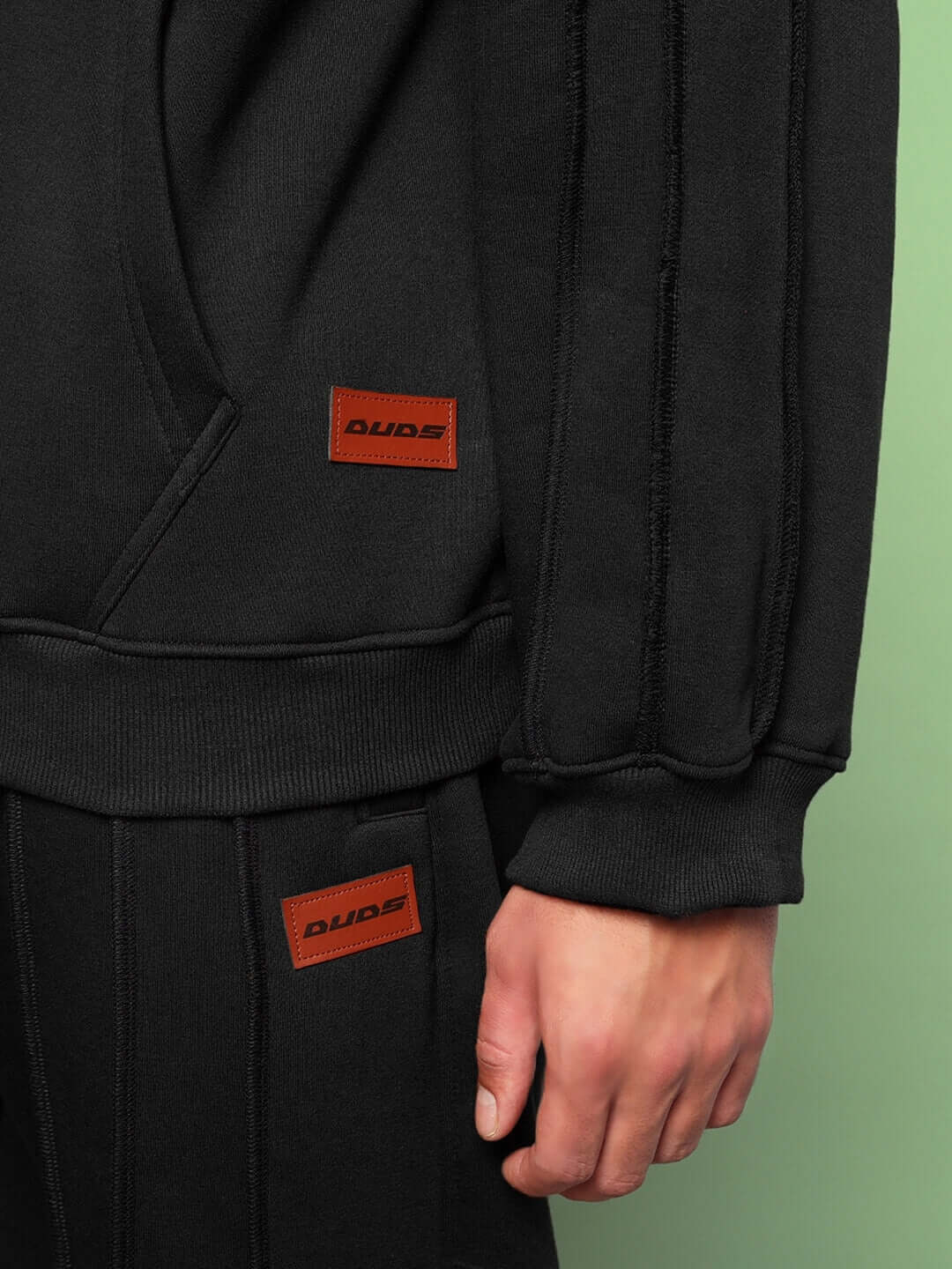 Close-up of URBAN SOLID PLATED FLEECE HOODIE BLACK showcasing premium fleece and plated detailing with bold patch labels.