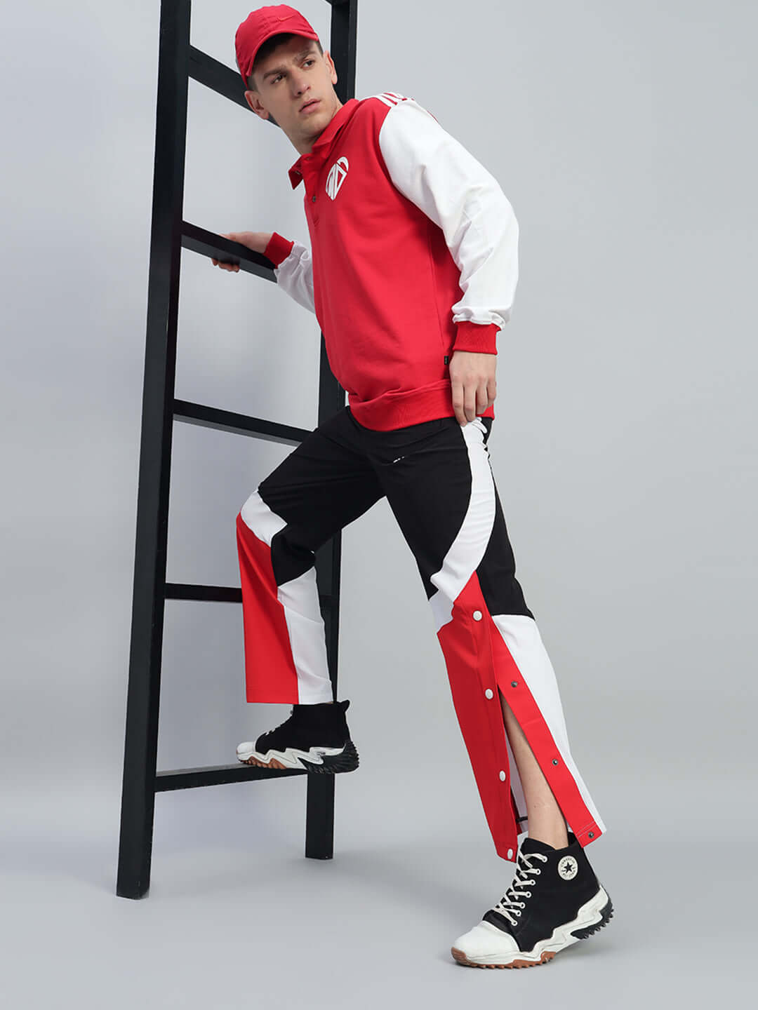 Model wearing MARCO RELAXED FIT CARGO PANTS BLACK RED with red and white athletic jacket on ladder.