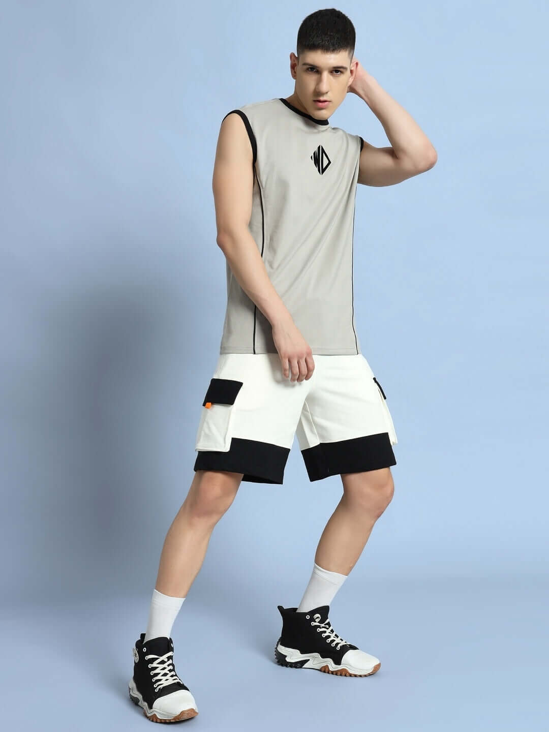 Man wearing off white-black utility cargo shorts styled with a sleeveless top, showcasing a modern and casual look against a plain background.