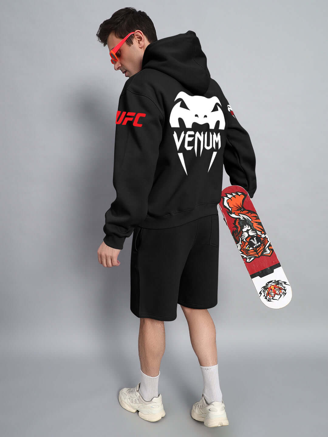 Man wearing WEARDUDS VENUM FLEECE HOODIE BLACK holding a skateboard with graphic design, showcasing stylish streetwear fashion.