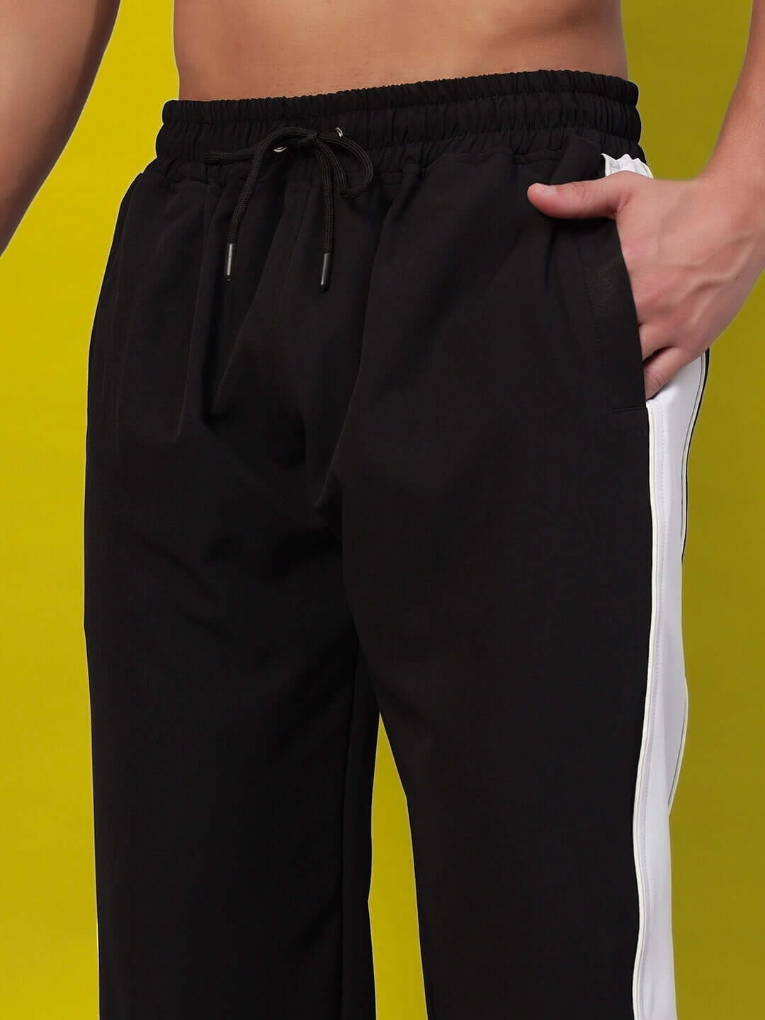 Black versatile parachute cargo pants with white side stripe, shown on a person standing against a yellow background.