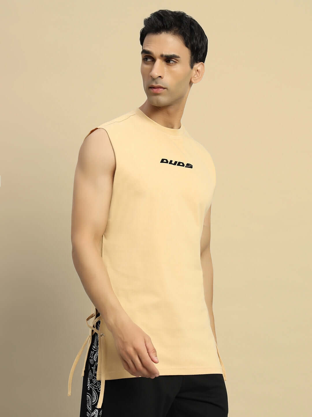 Model wearing Vertex Relaxed Fit Sleeveless T-shirt in beige by DUDS, featuring a casual design ideal for custom fit options.