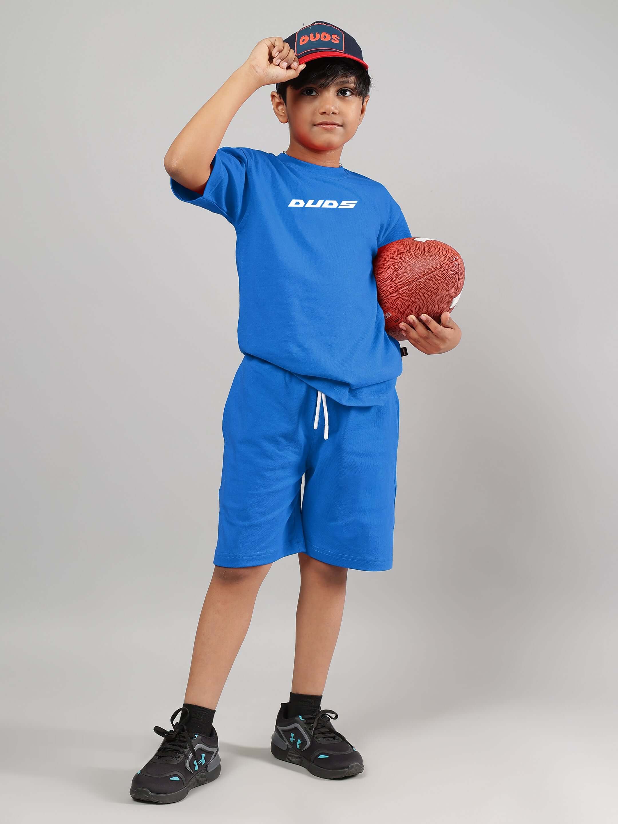 Boy wearing VICTORY co-ord set in royal blue and holding a football, promoting unisex casual wear by DUDS.