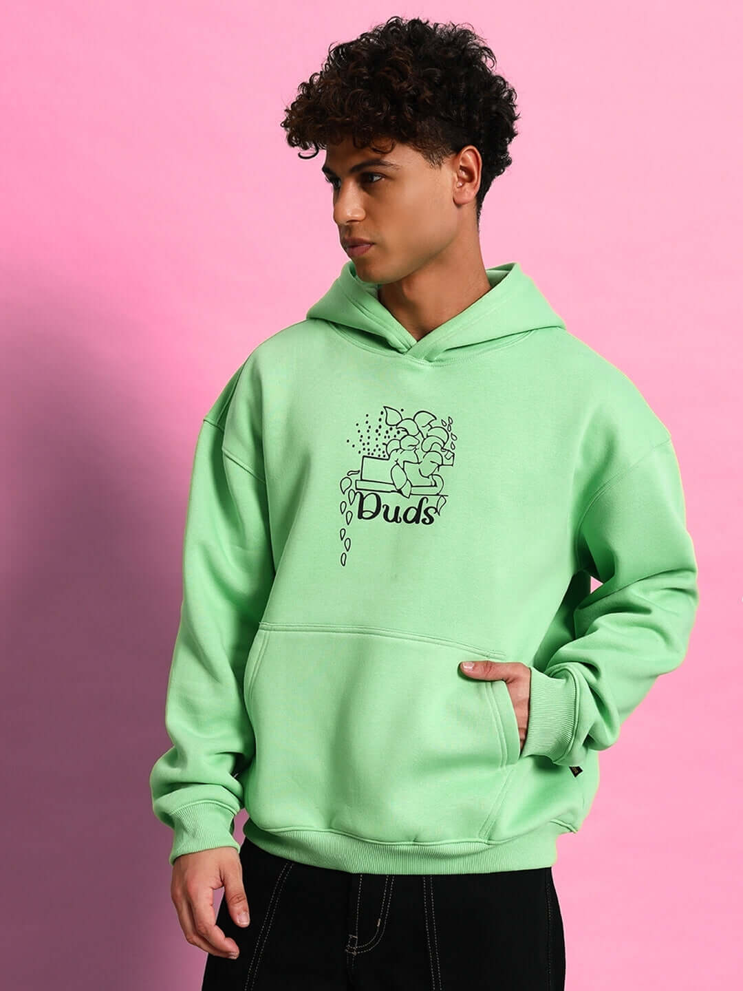 Person wearing VOODO OVERSIZED FLEECE HOODIE GREEN with streetwear style on pink background.