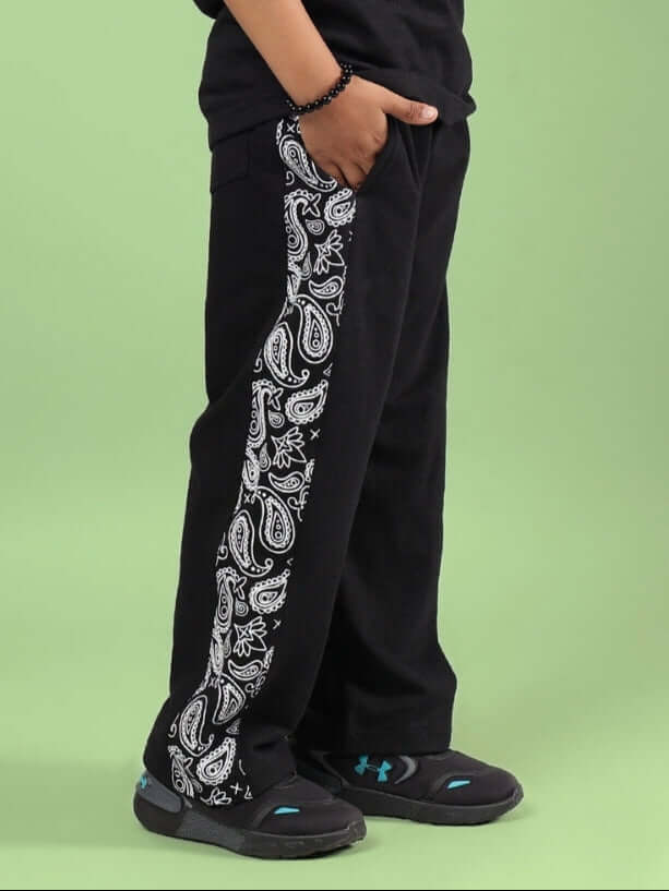 Child wearing WALTZ JOGGER FOR BOYS & GIRLS BLACK with paisley pattern side panel for sporty style and comfort on green background.