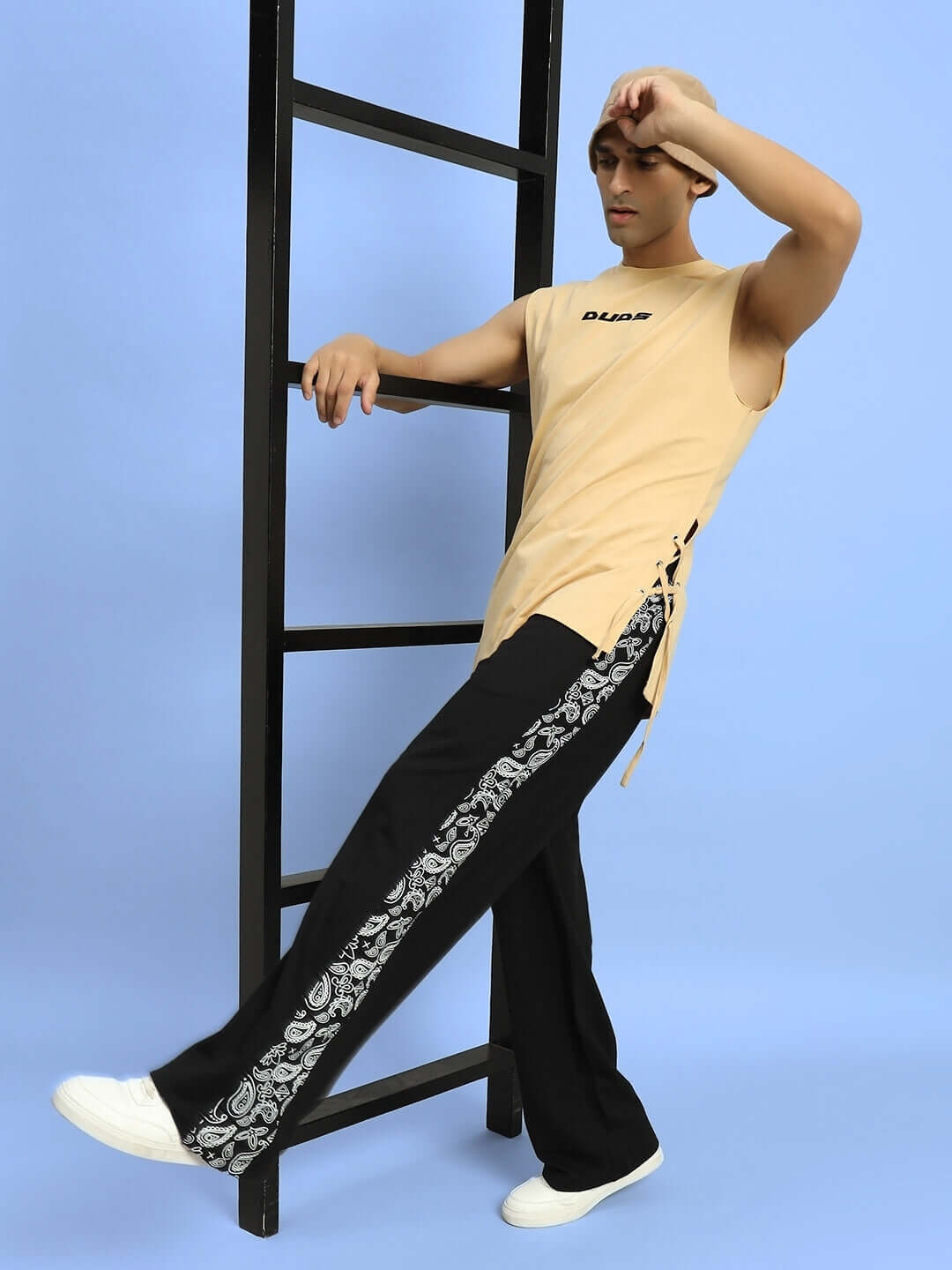 Model wearing WALTZ relaxed fit black joggers with printed side stripe, styled with a beige sleeveless top, leaning on a ladder.