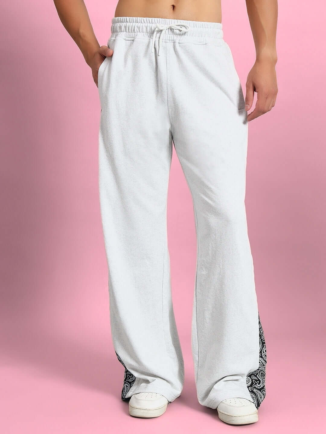 Person wearing WALTZ relaxed fit joggers in mélange grey, standing against a pink background, showcasing casual style.