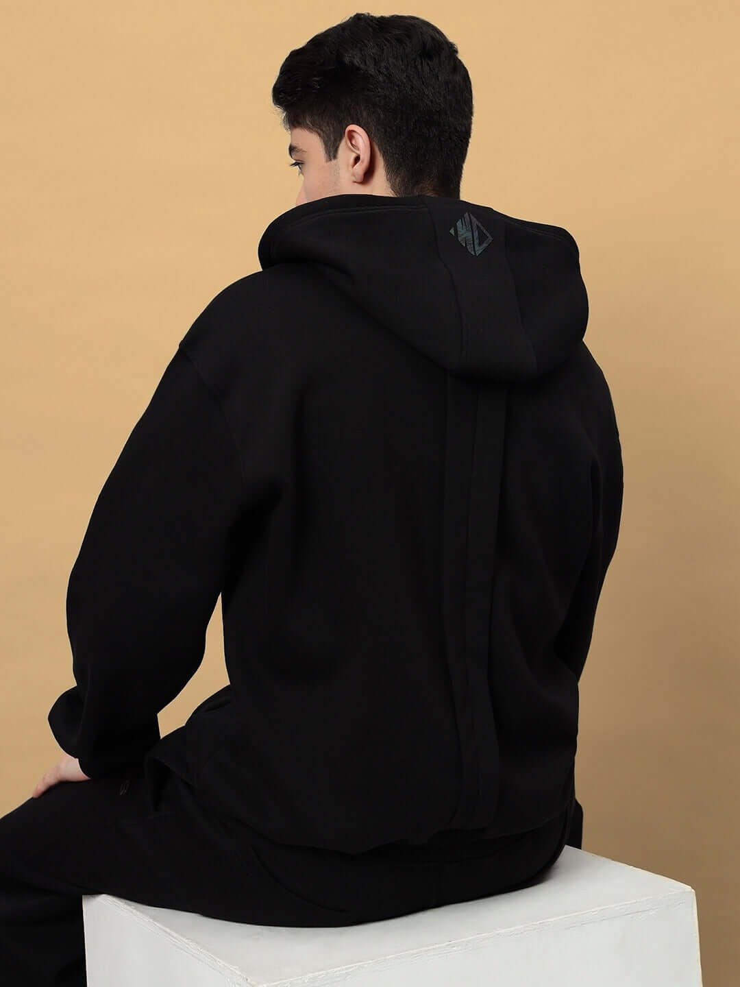 Rear view of a model wearing a WD ADMIRE COTTON FLEECE HOODIE BLACK featuring an oversized fit and ribbed trims.