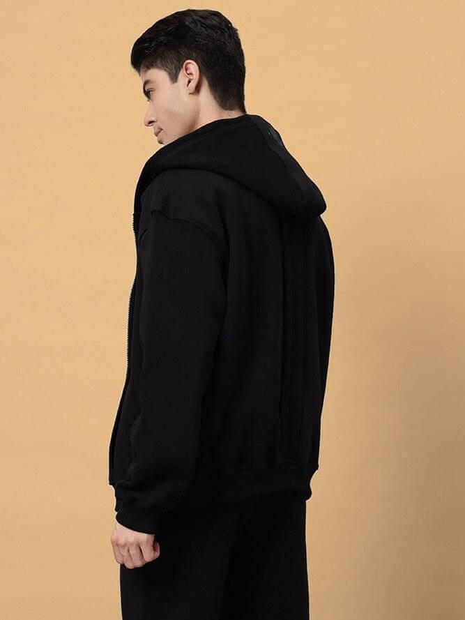Person wearing WD ADMIRE COTTON FLEECE HOODIE BLACK from the back, showing spacious hood and relaxed fit on light brown background.