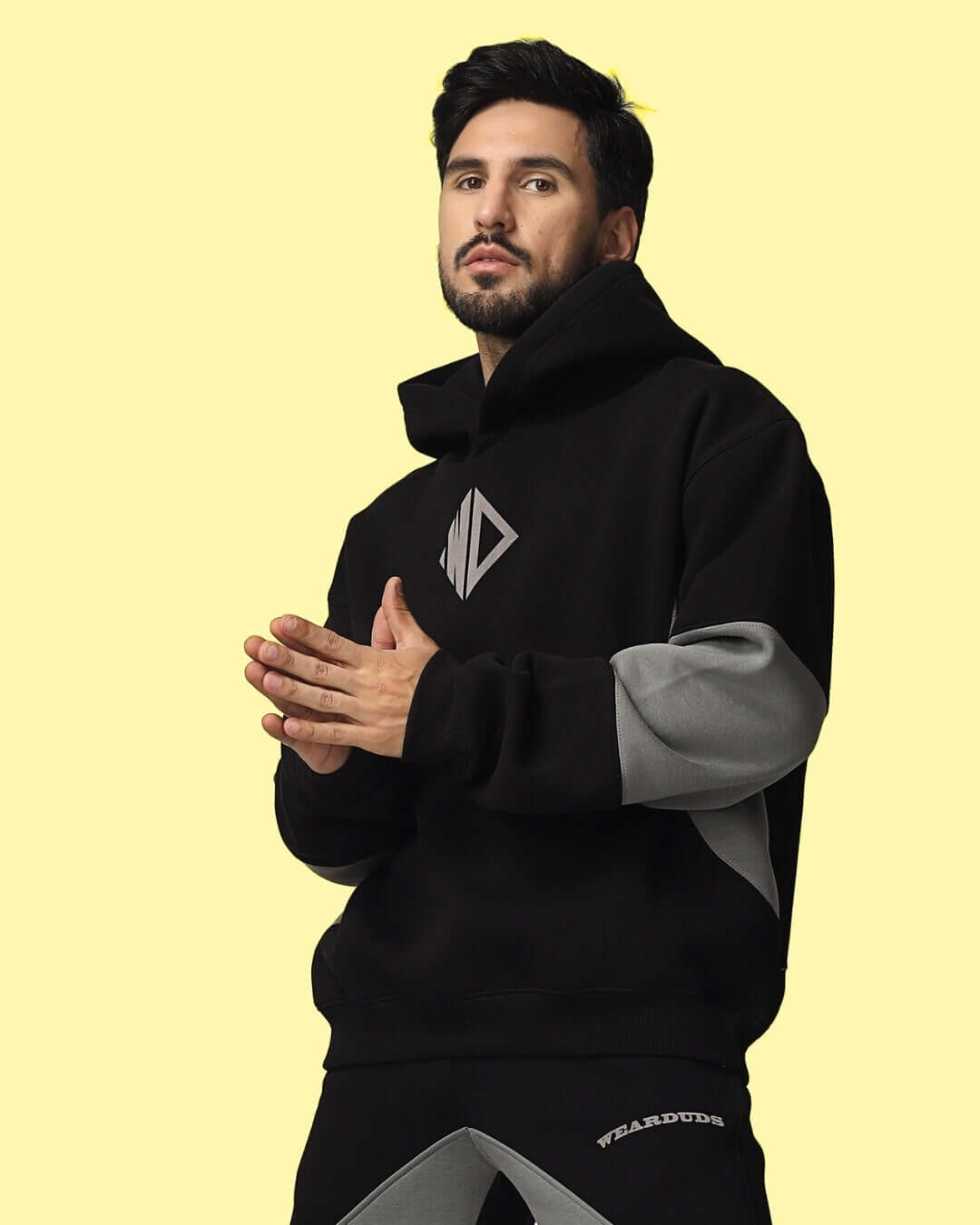 WD Gorpcore Colorblock Hoodie in black and grey, featuring distinctive colorblocking design, worn by model on a yellow background.