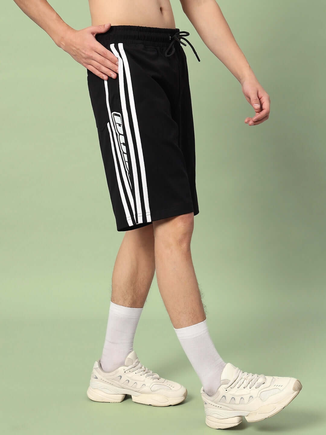 Man wearing WD Premium Regular Fit Black Shorts with custom fit option and white sneakers, showcasing sporty style.
