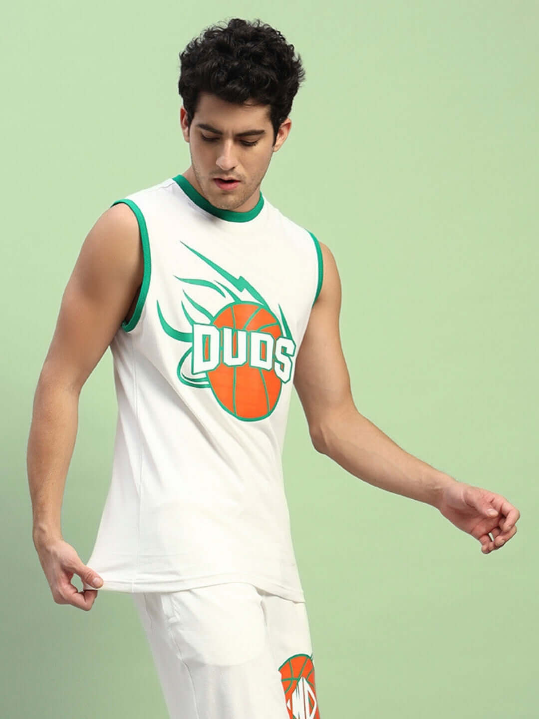 Model wearing a white sleeveless t-shirt with green trim and basketball graphic, styled with matching shorts, on a green background.