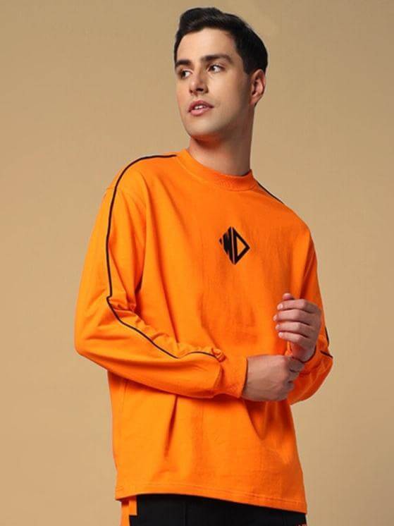 Model wearing orange oversized sweatshirt made from premium cotton French Terry, featuring black stripe detail and logo. Casual fashion.