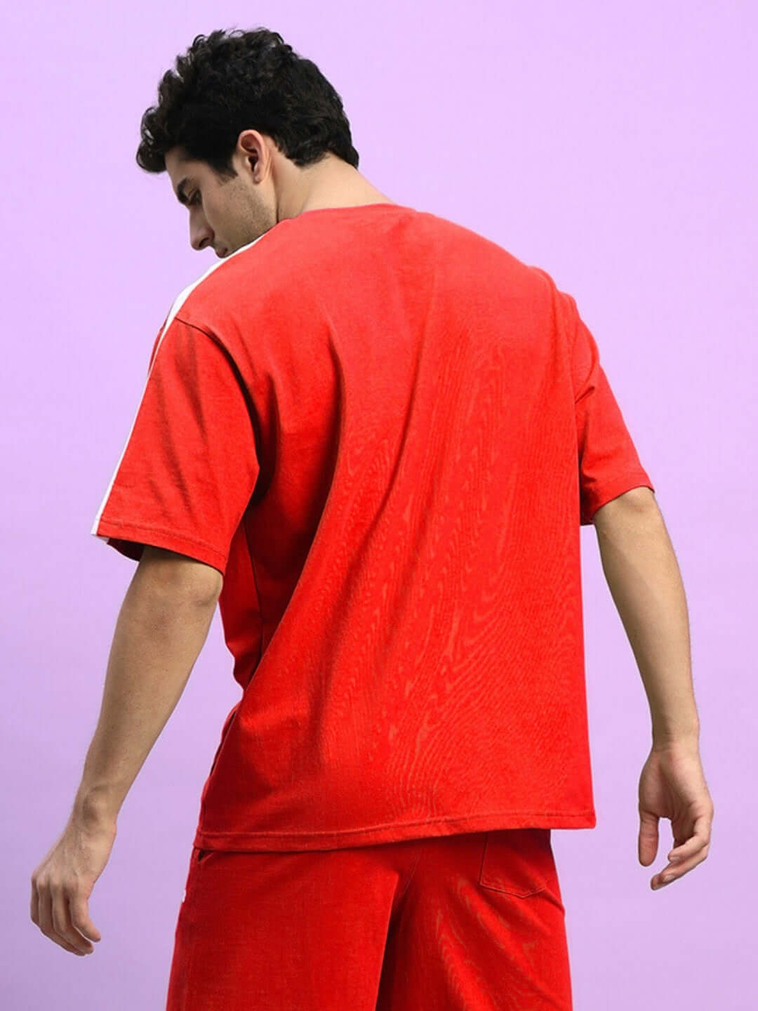Back view of a man wearing a red oversized Wideline T-shirt, made from premium cotton French terry with elastane, against a purple background.