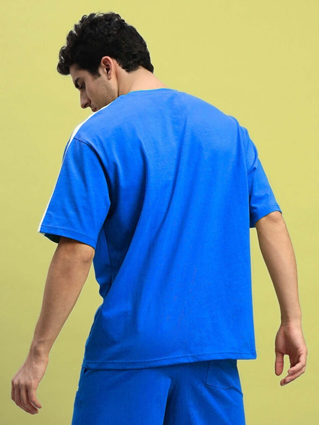 Man wearing royal blue oversized T-shirt made of premium cotton, showcasing back view, vibrant color in contrast to light background.