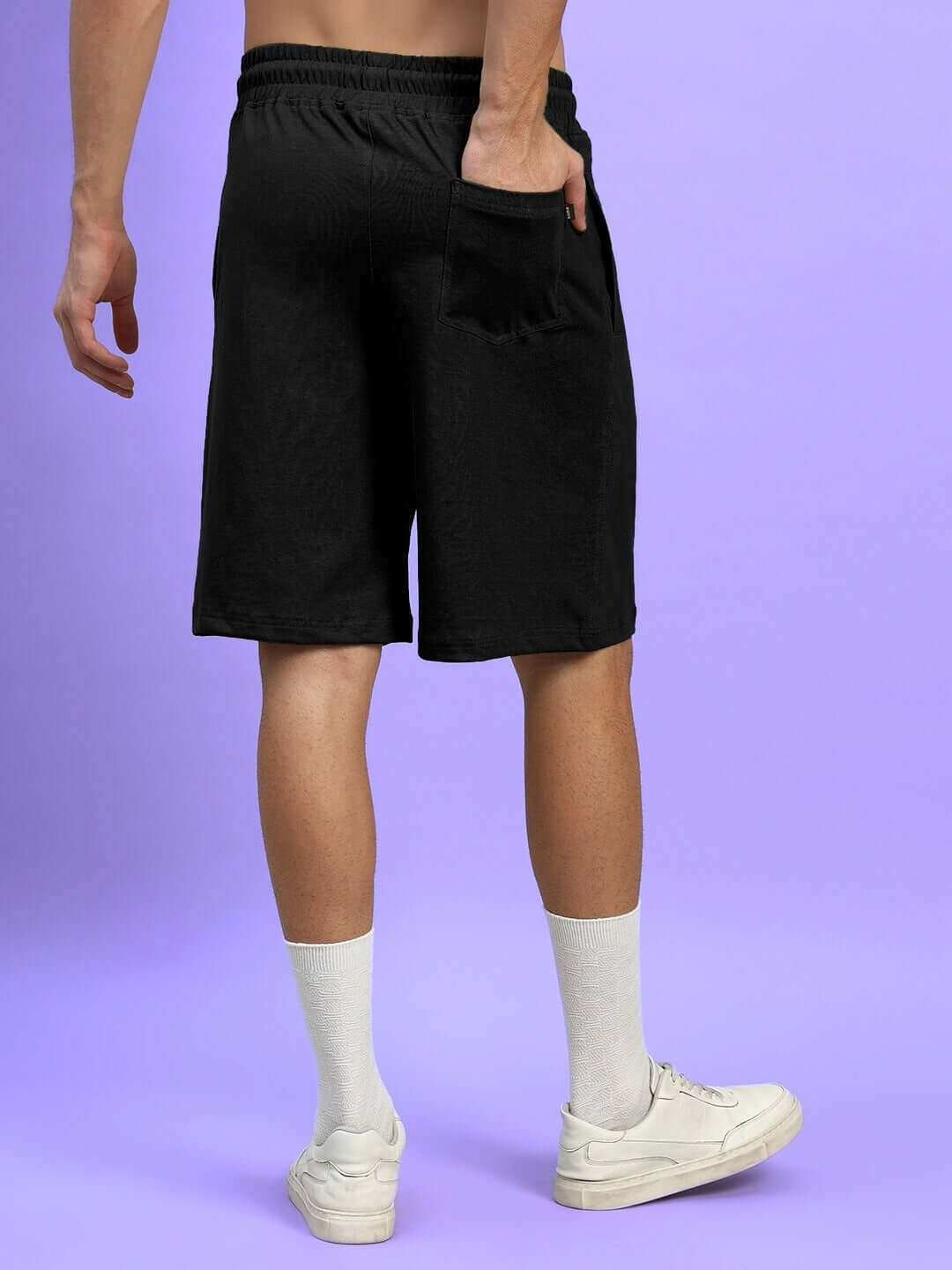 Back view of WIDELINE Regular Fit Black Shorts, showcasing pocket detail, worn by male model standing against a purple background.