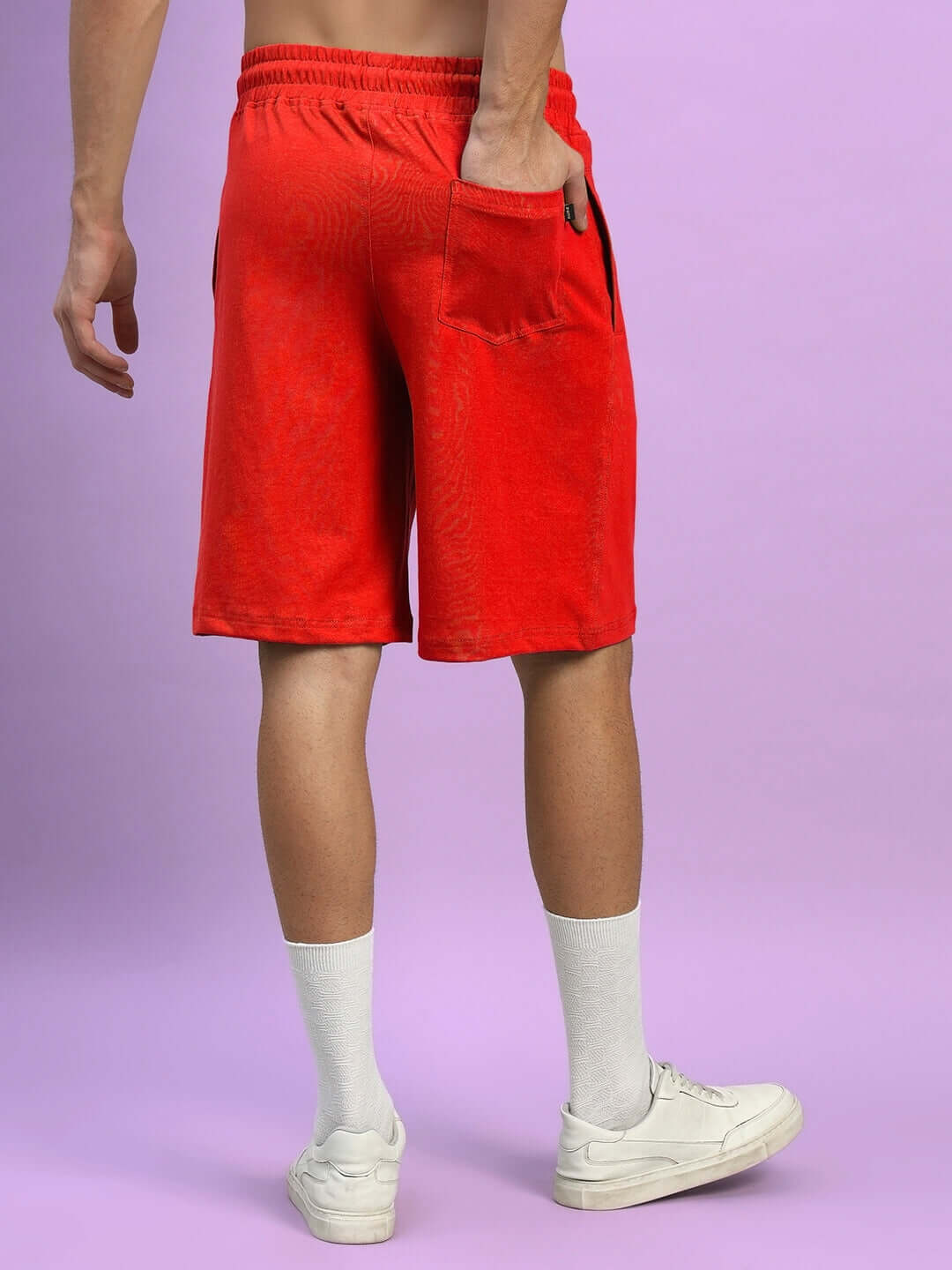 Back view of a person wearing Wideline Regular Fit Red Shorts with pocket detail, showcasing casual style against a purple background.