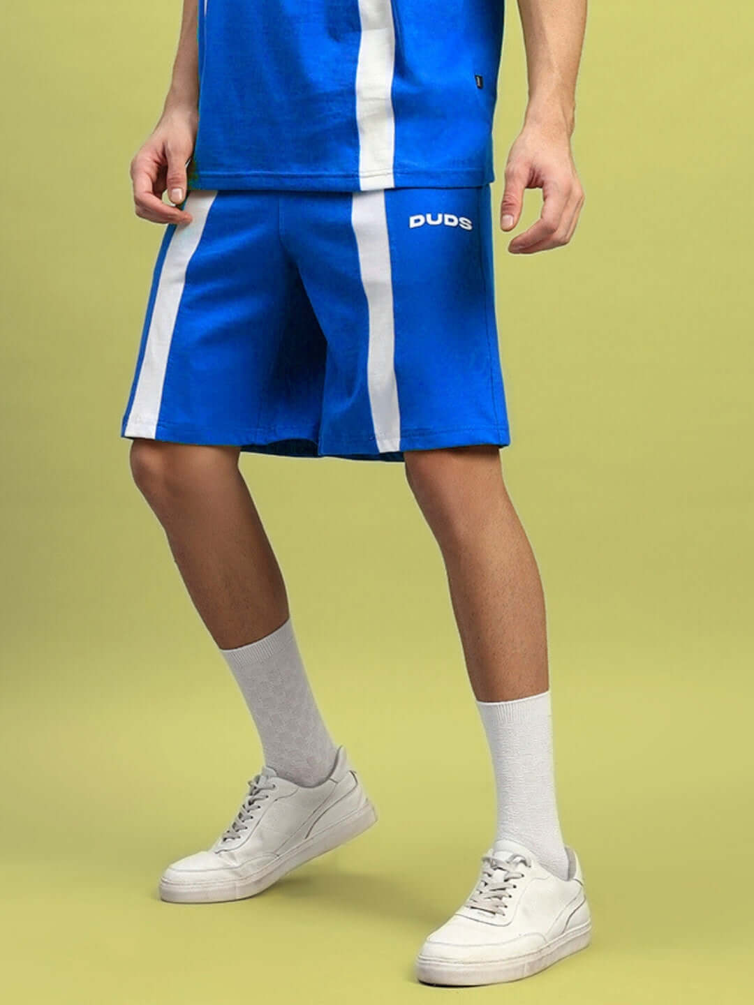 Person wearing WIDELINE REGULAR FIT SHORTS ROYAL BLUE with white sneakers on a green background