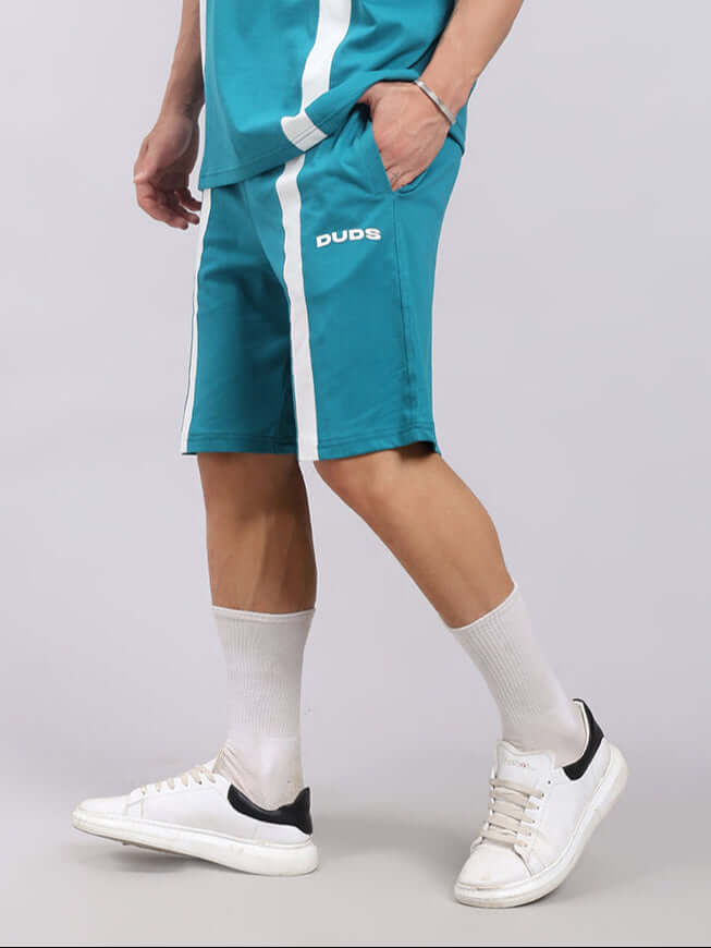 Person wearing WIDELINE REGULAR FIT SHORTS TEAL, showing side view with striped detailing. Ideal for casual or sporty looks.